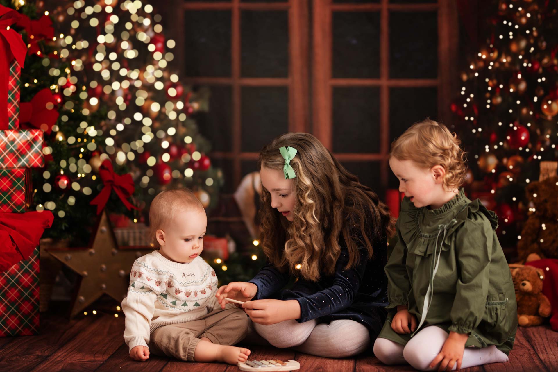 Christmas Photoshoot Oxfordshire Two girls and a boy play with a toy xylophone whilst having their Christmas photos taken