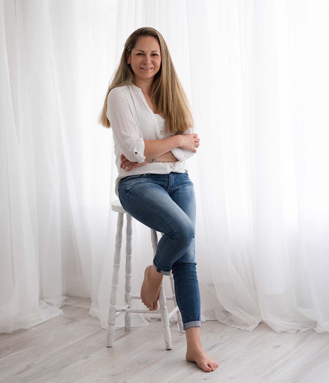 Professional-Headshots-Chipping-Norton Professional women wearing blue jeans and a white blouse posing on a wooden stool for her business headshots