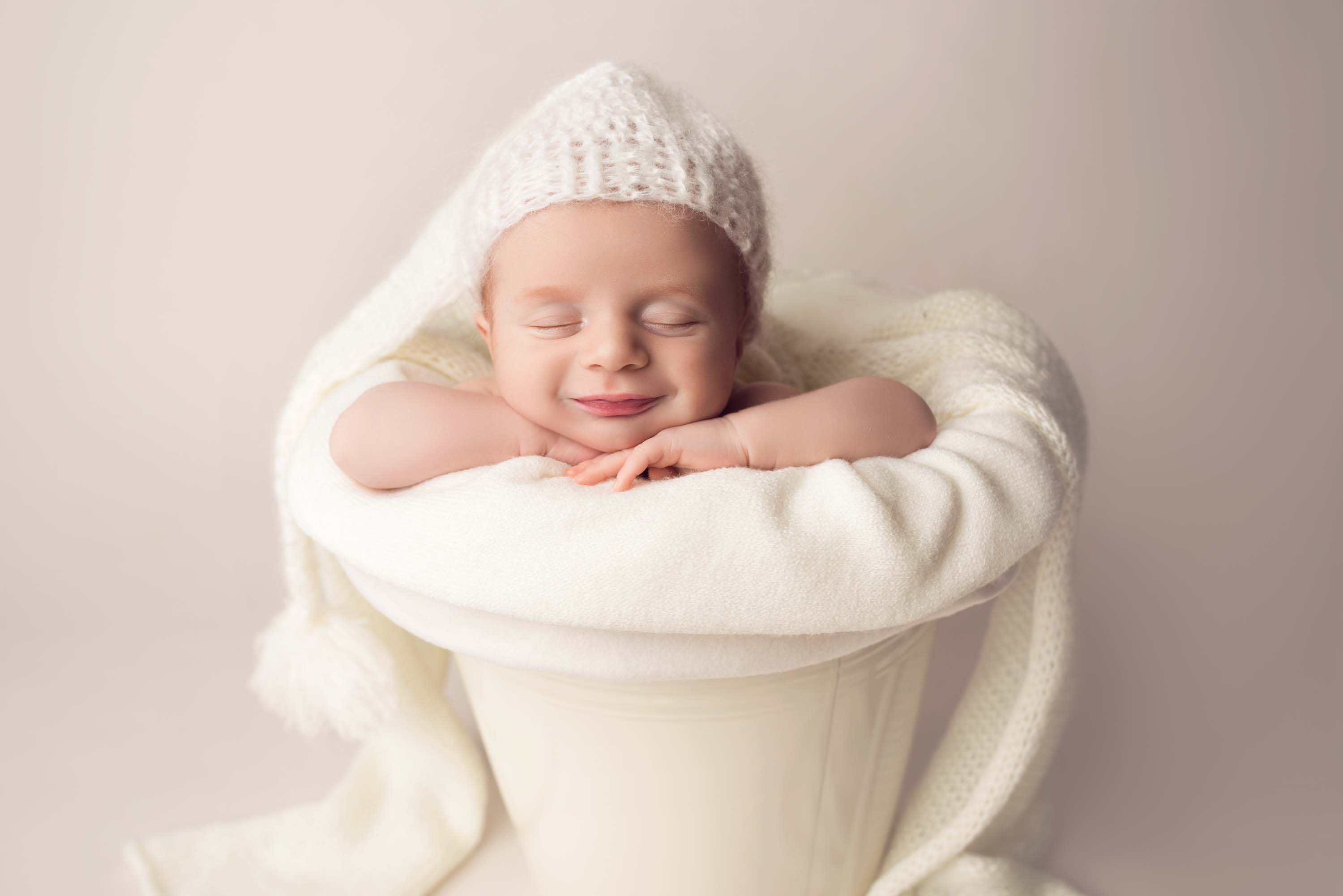 Baby boy asleep in a bucket wearing a sleeping hat and a big smile