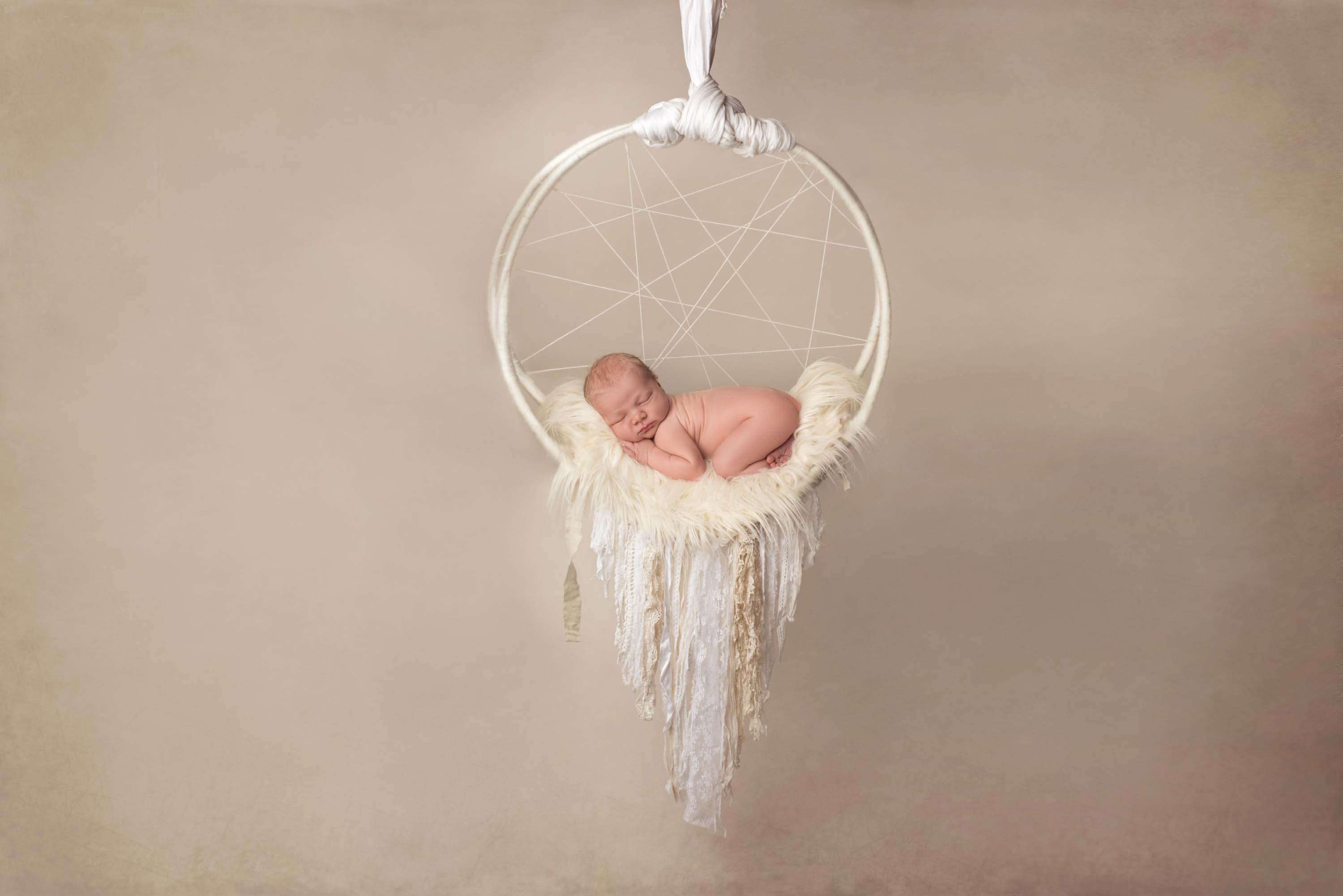 Week old baby boy suspended in the air lying in a dreamcatcher