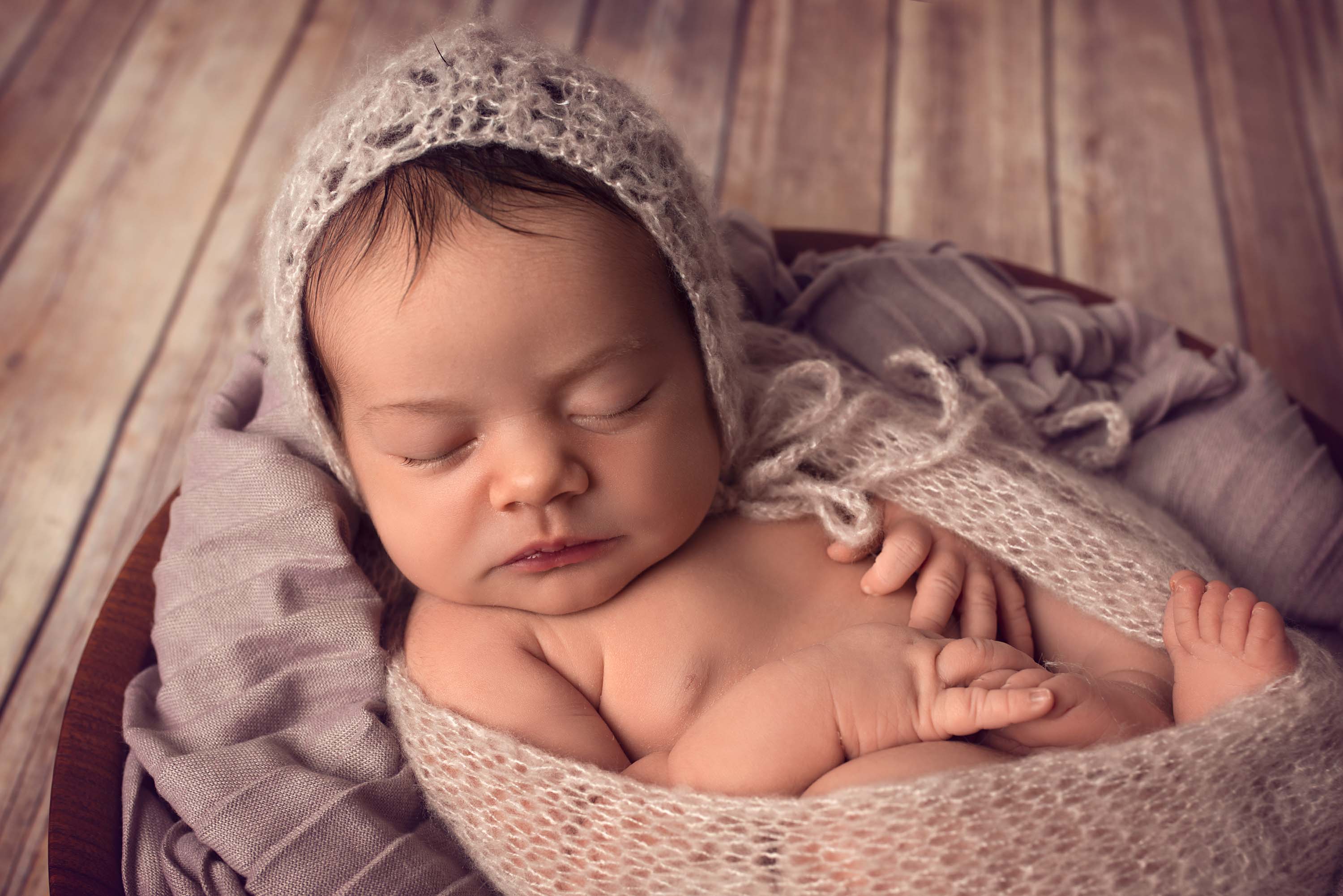 Baby asleep in a bowl on wooden floorboards for her baby photoshoot
