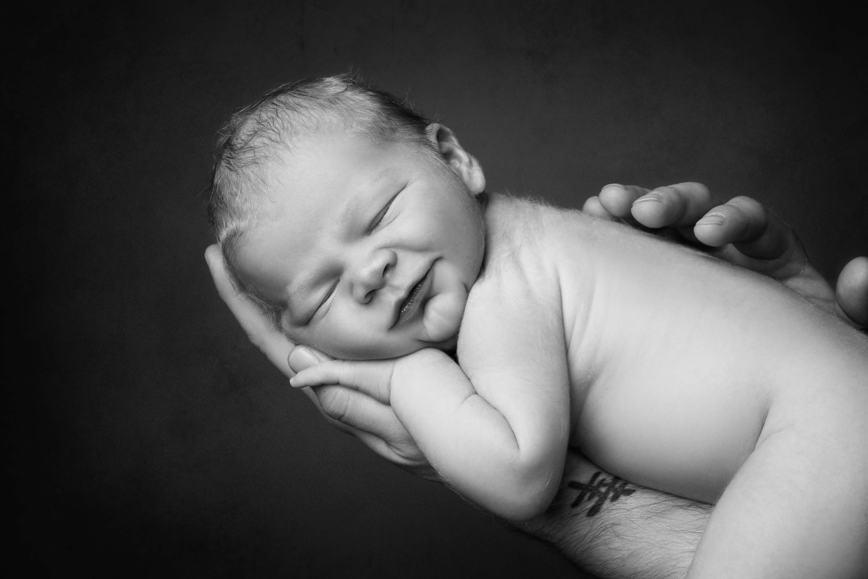 Smiling newborn baby boy asleep on his father's arm