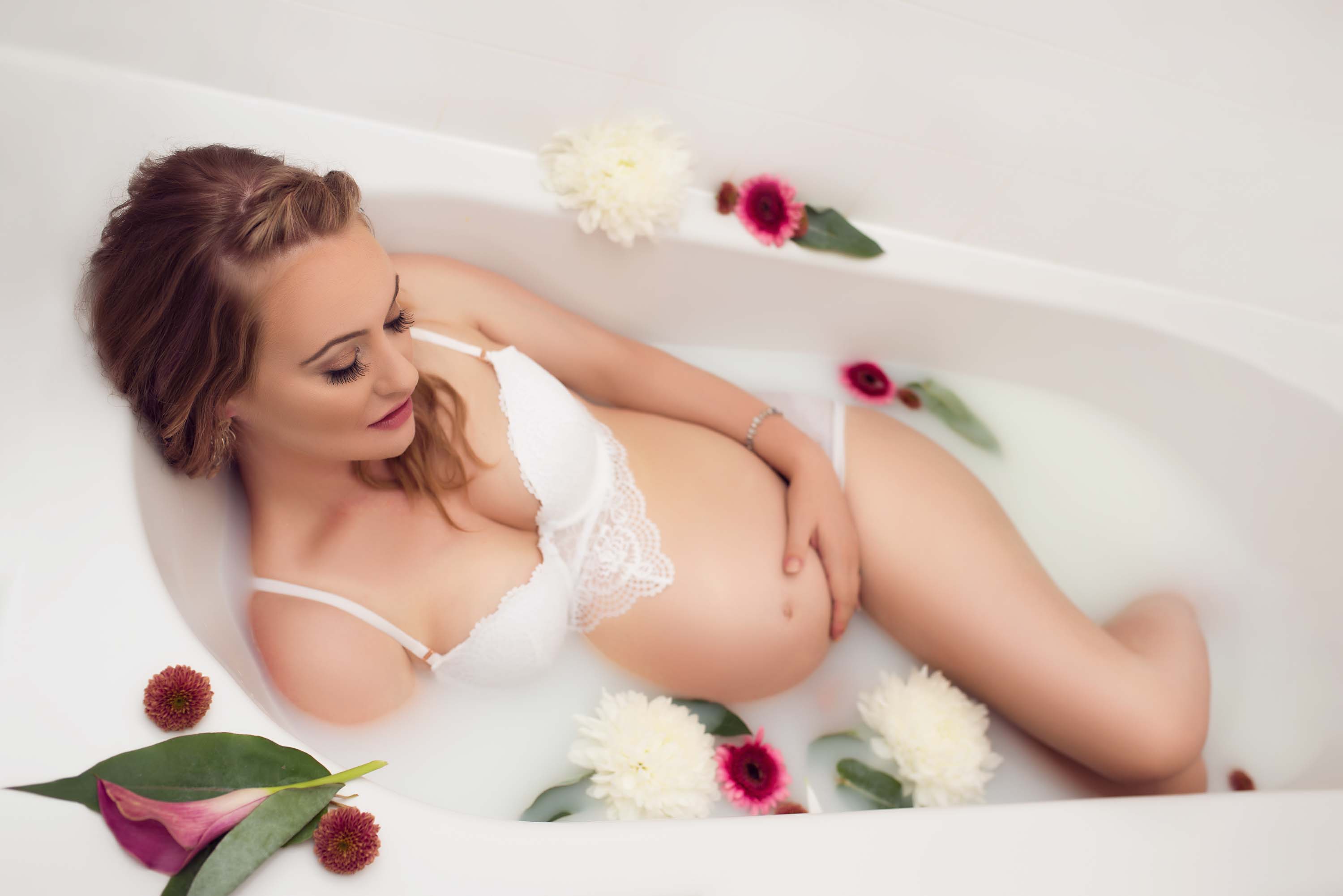 Lady with baby bump in milk bath with purple and white flowers