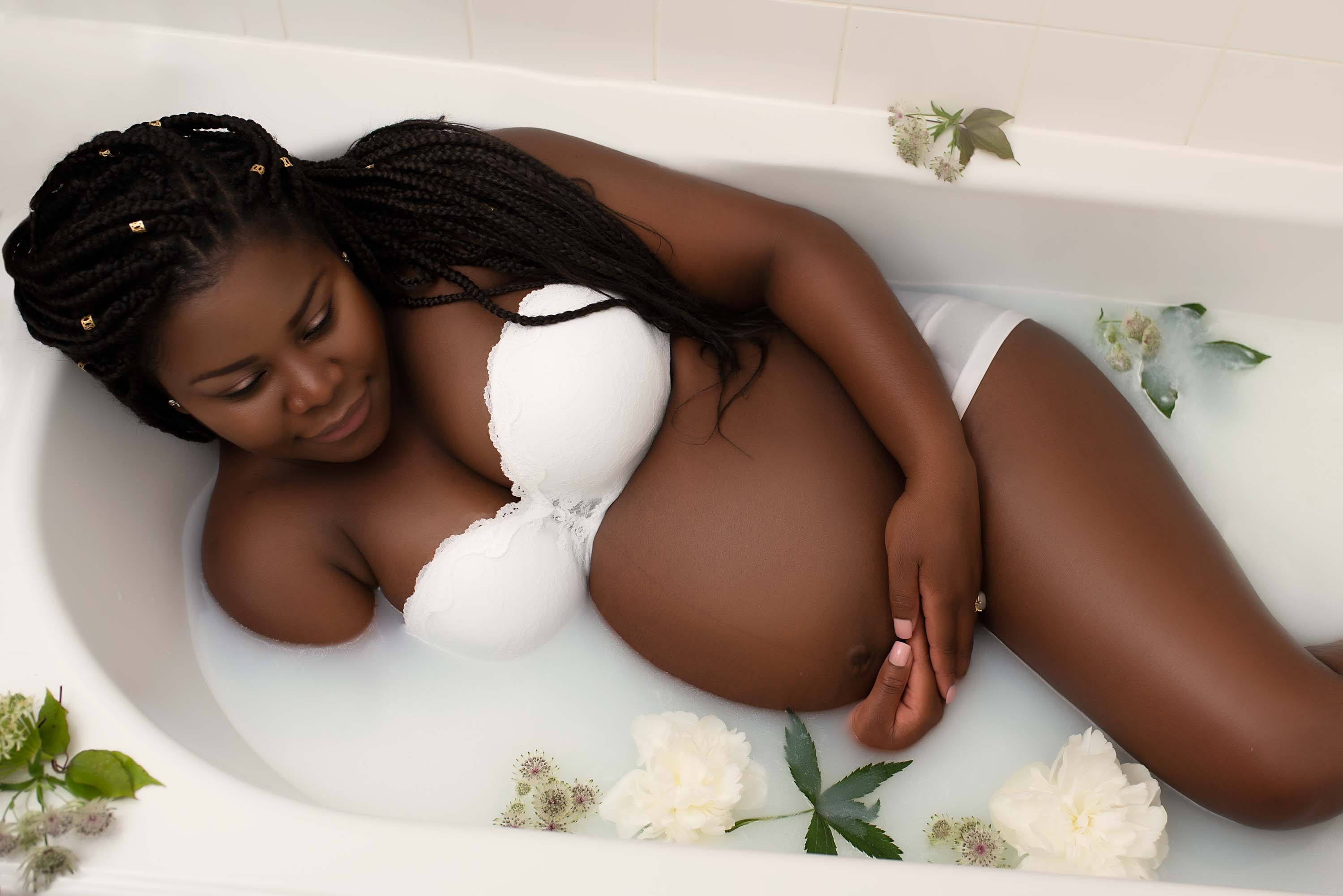 Women lying in milk bath with flowers for pregnancy photo shoot
