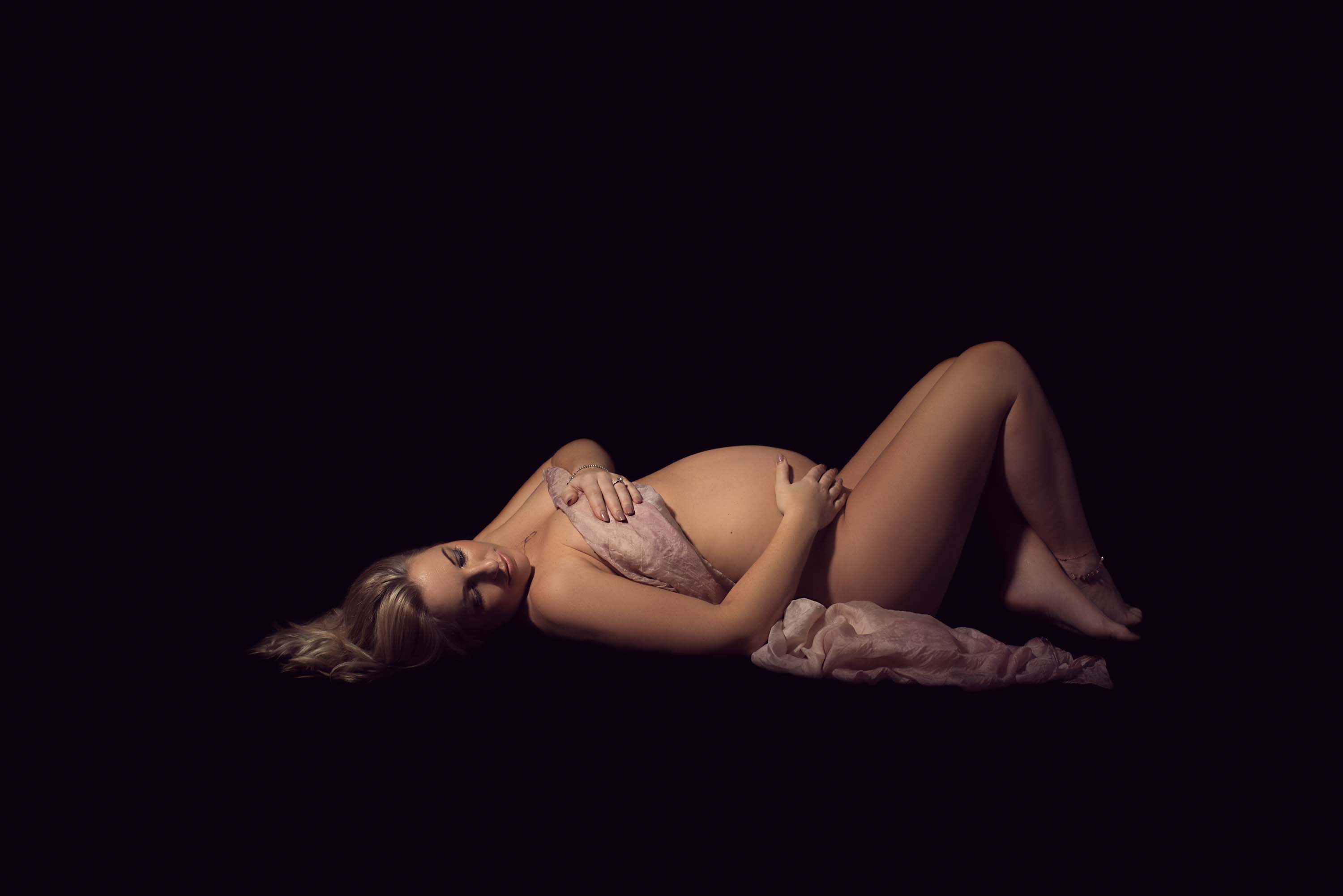 Pregnant photoshoot of lady lying on floor with black background