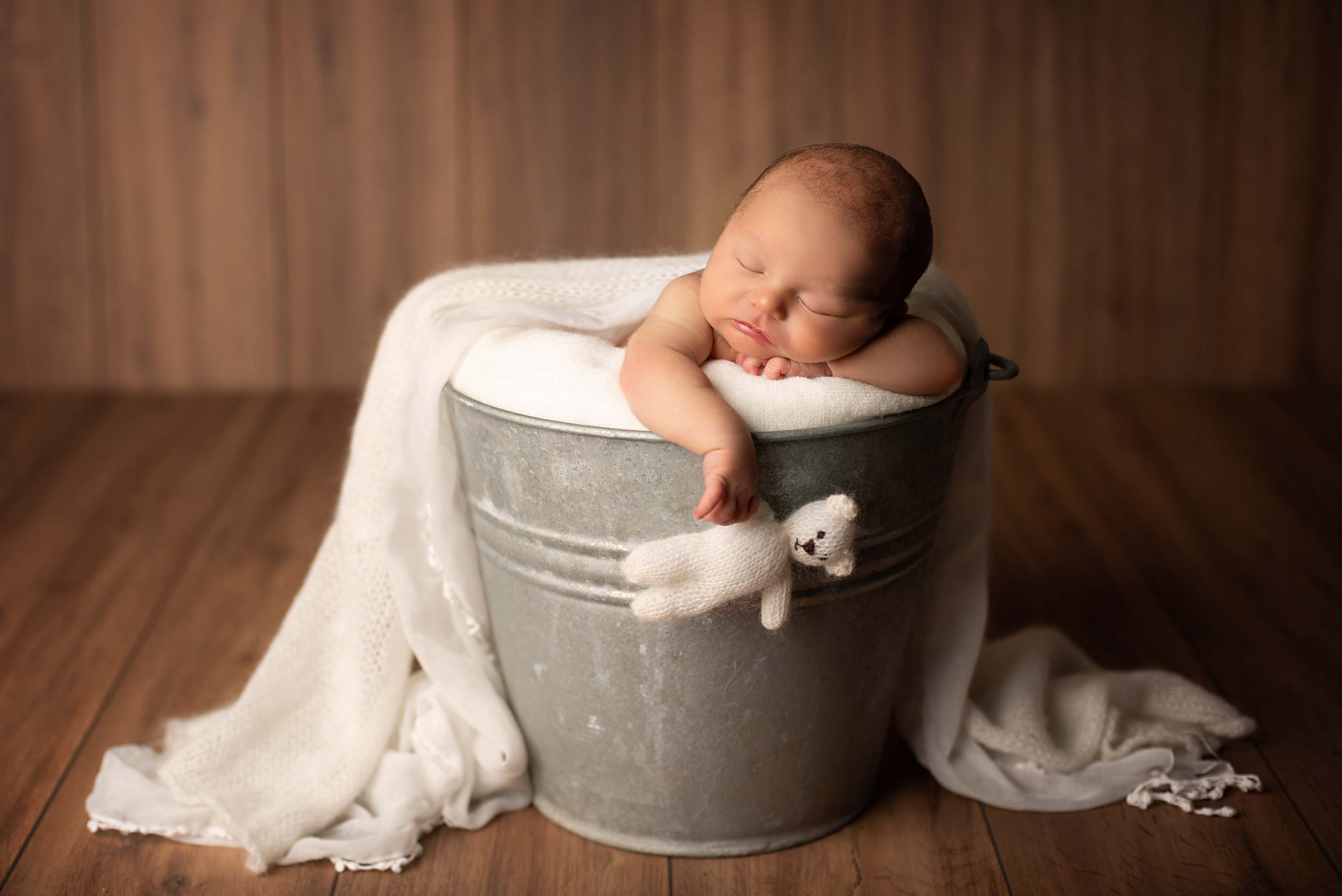 Baby boy asleep in a galvanised bucket holding on to a teddy