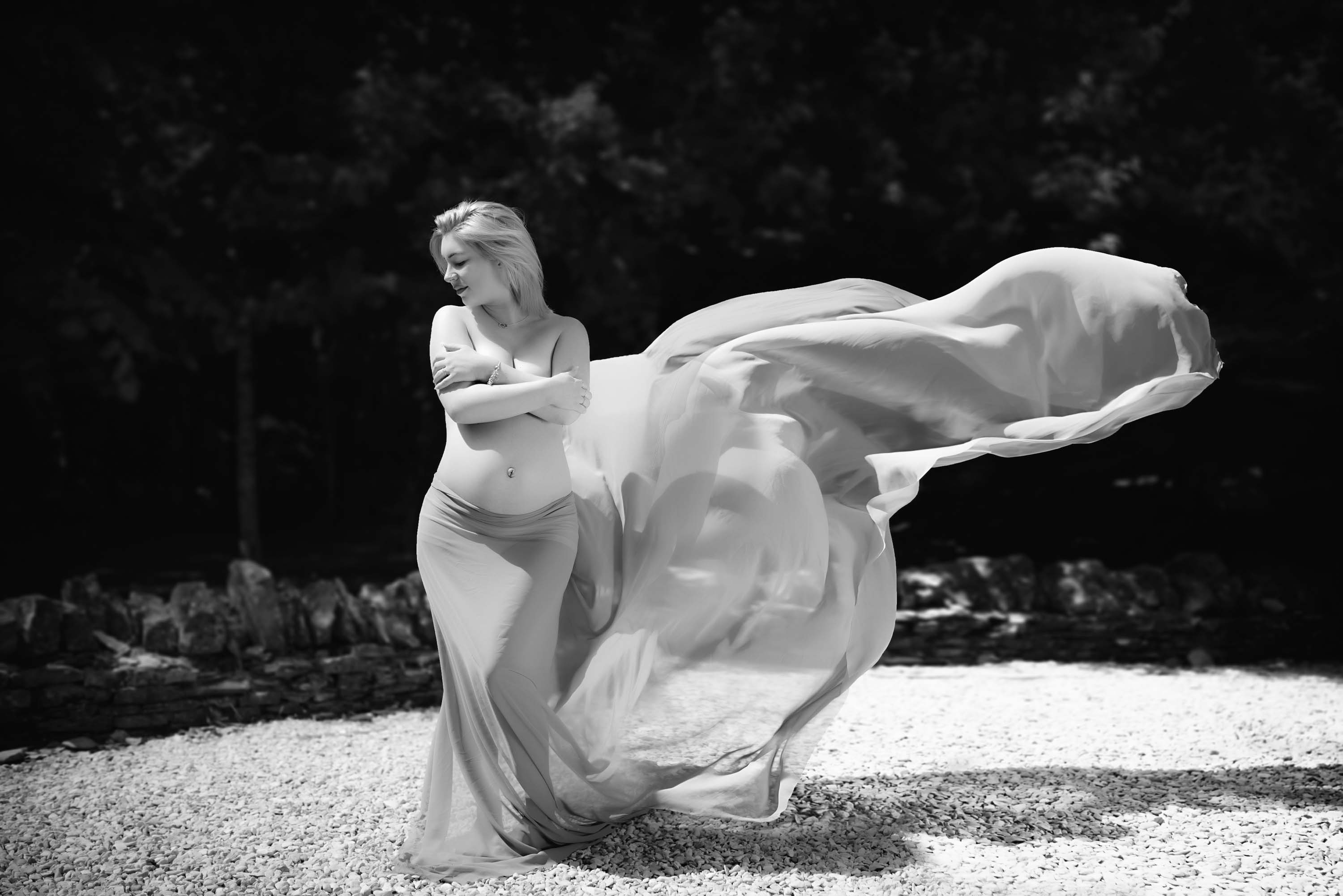 Pregnant women standing in gravelled courtyard with her maternity gown blowing in the wind