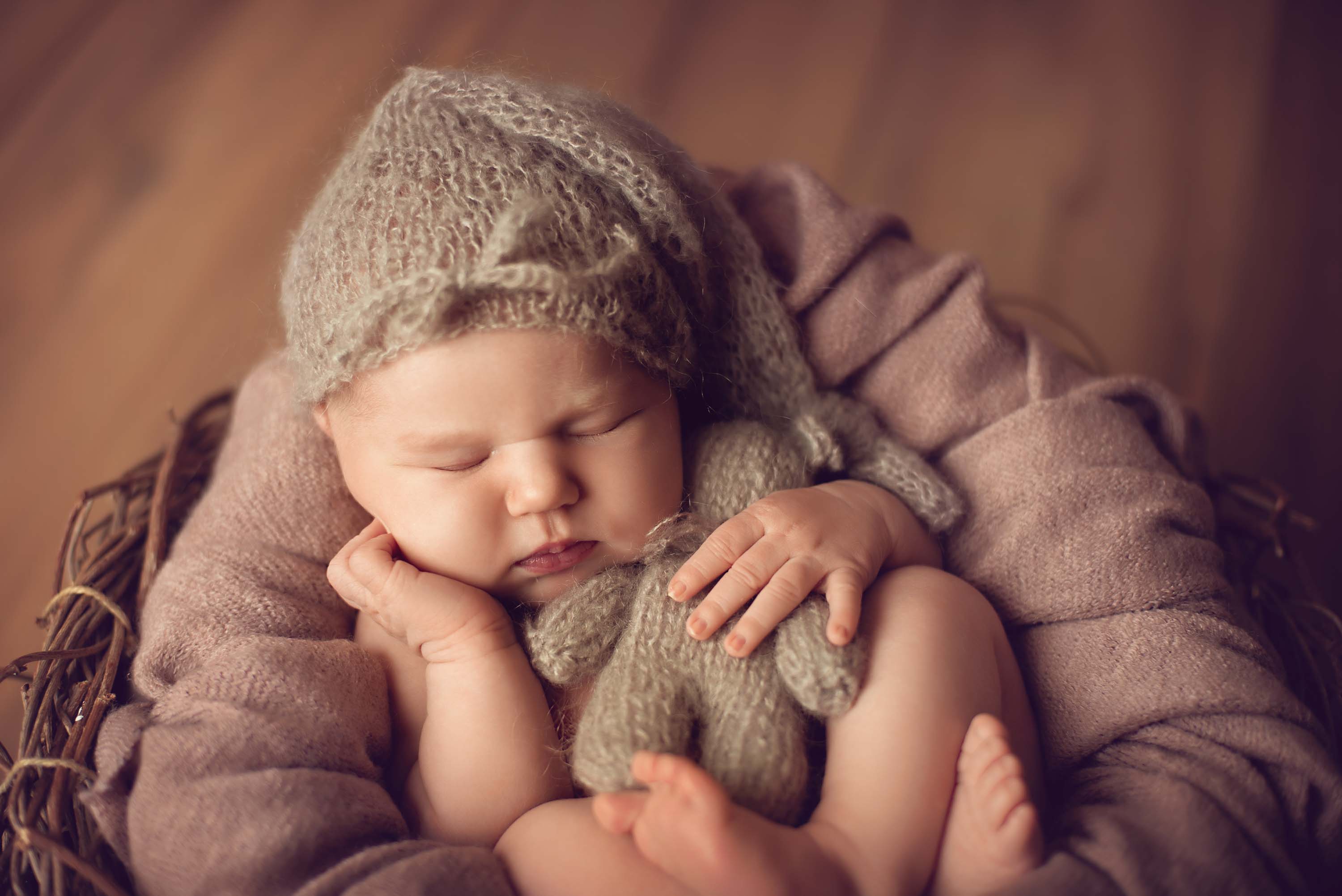 Week old baby wearing sleeping cap and cuddling a teddy in a basket