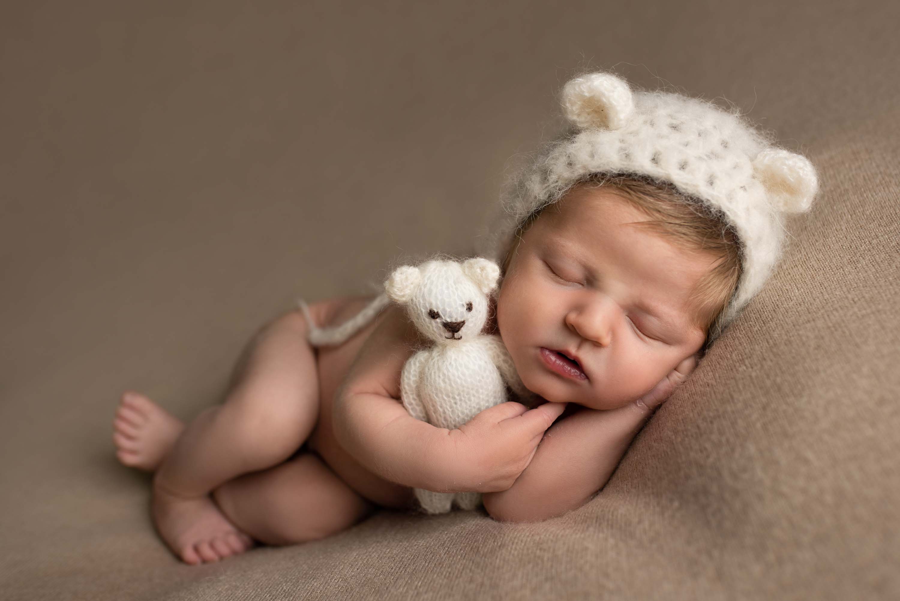 Baby boy in side pose wearing knitted bear hat and cuddling a little teddy bear