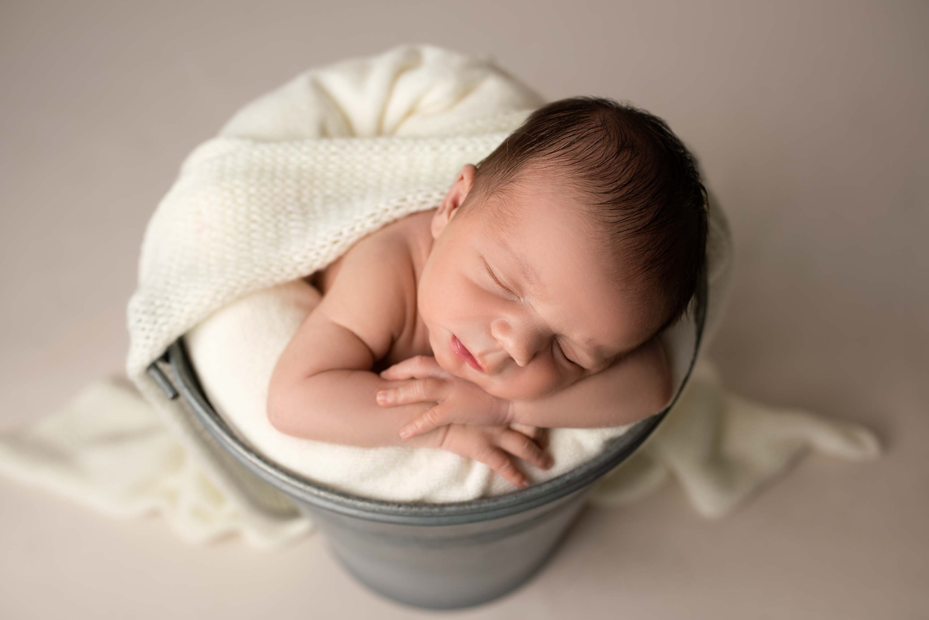 Newborn boy asleep in a metal bucket photographed from above