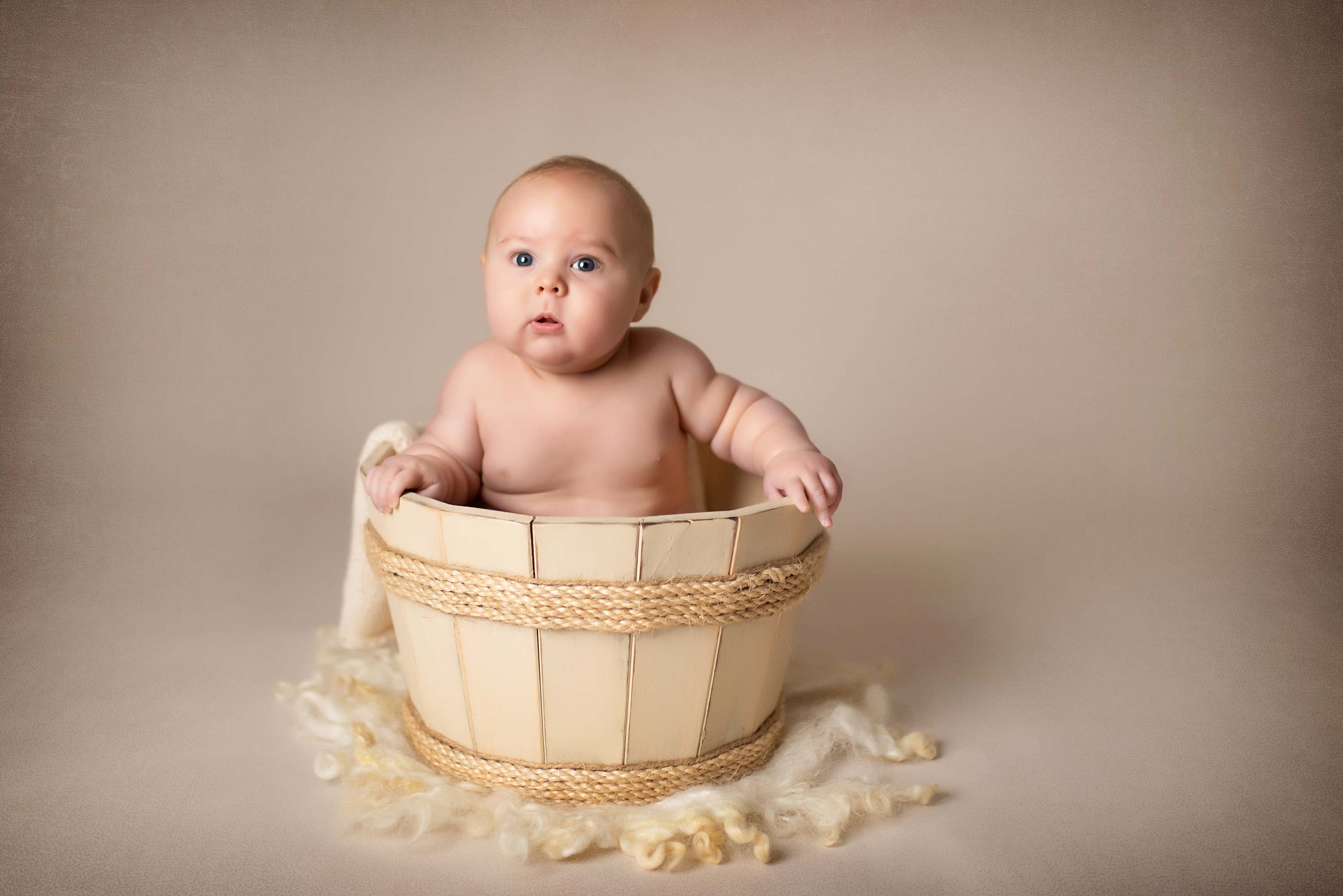 4 month old boy sitting in a wooden barrel for his baby photos