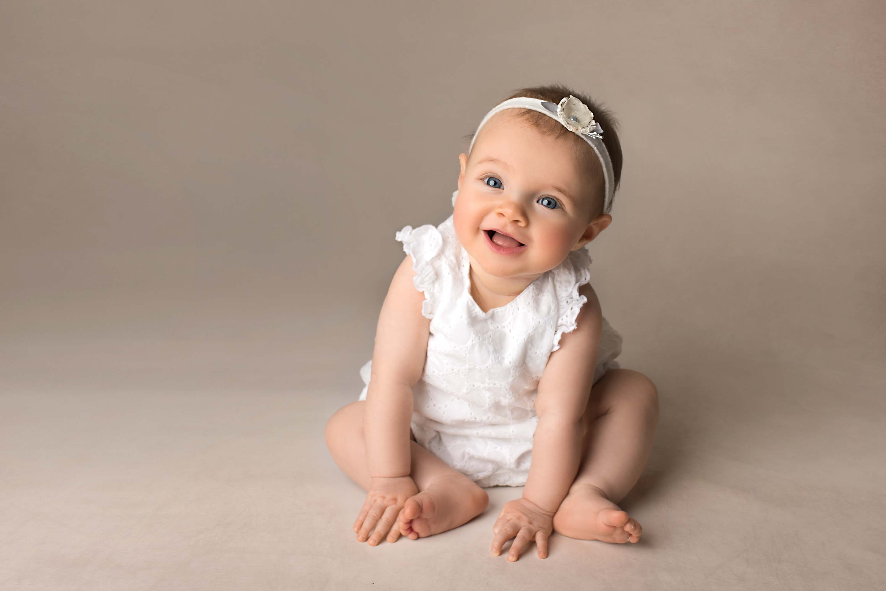 Young girl sitting on floor wearing white romper and headband