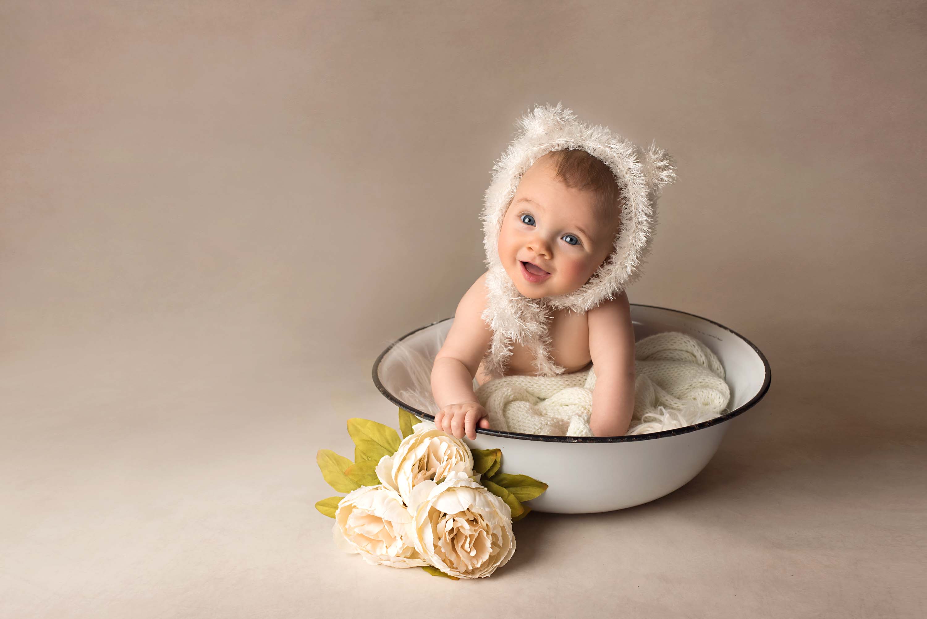 Baby girl with big blue eyes wearing bear hat and sitting in a bowl