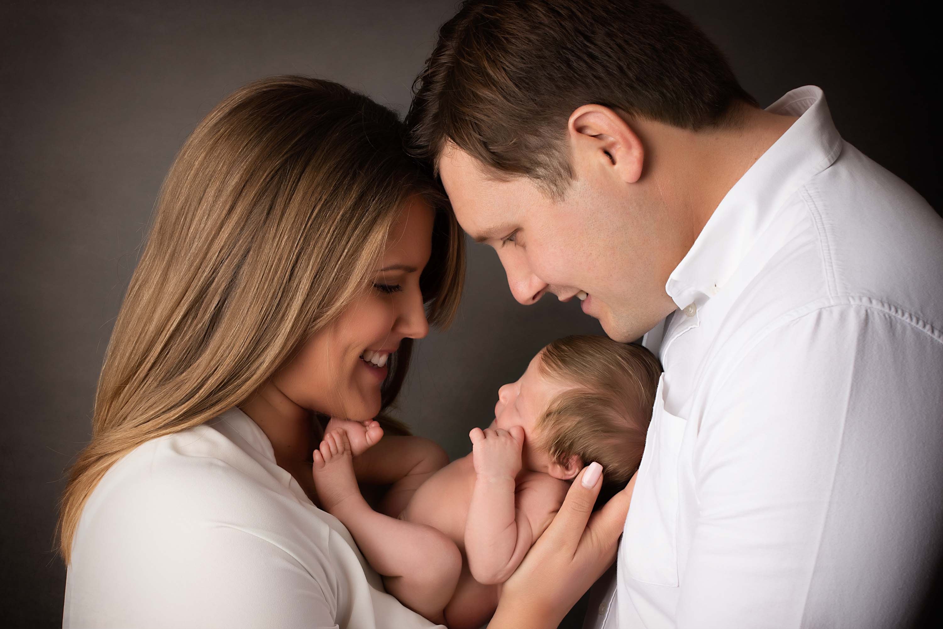 Baby boy nestled in between mother and father during their baby photoshoot