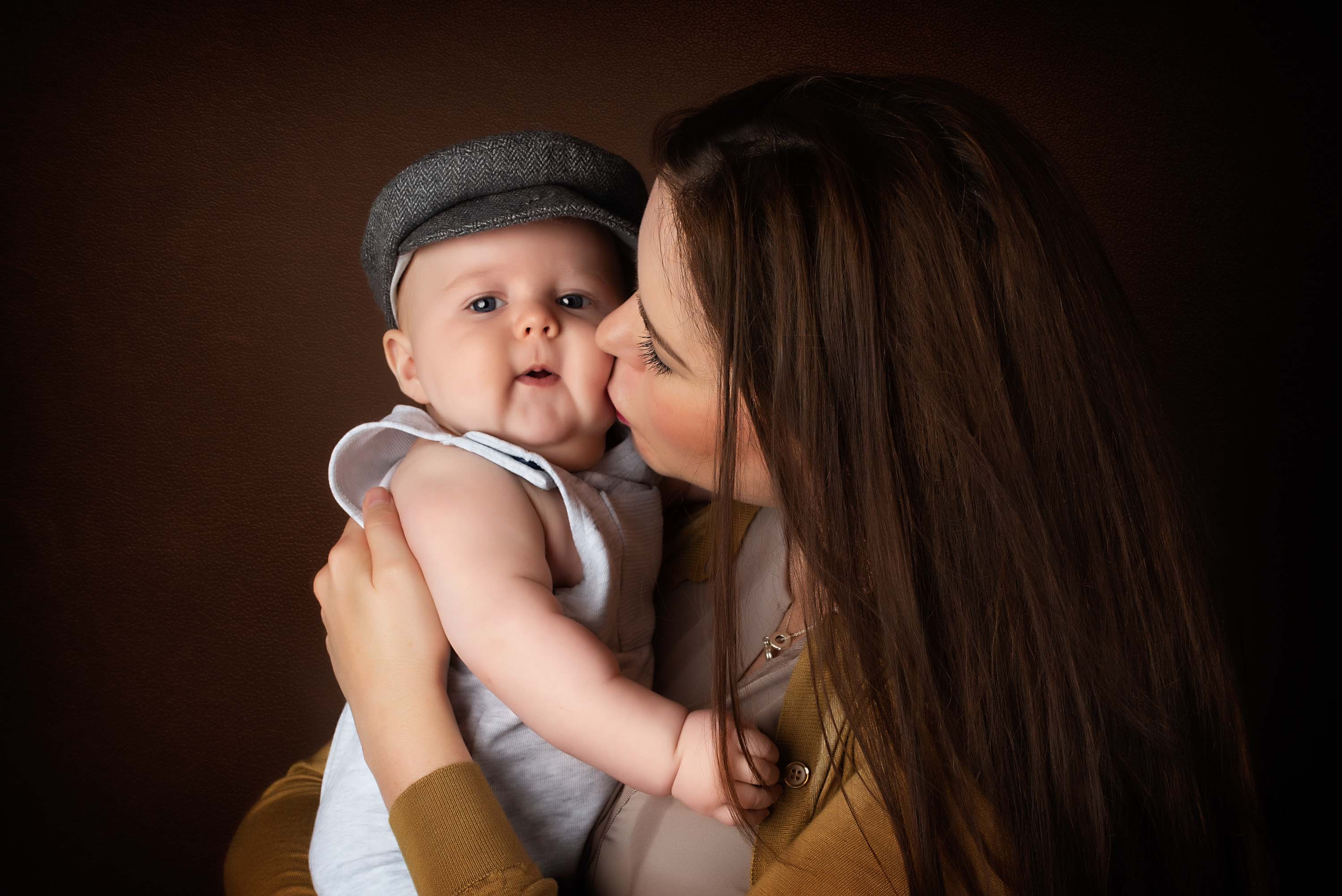 Mother kissing her 4 month old son wearing a flat cap