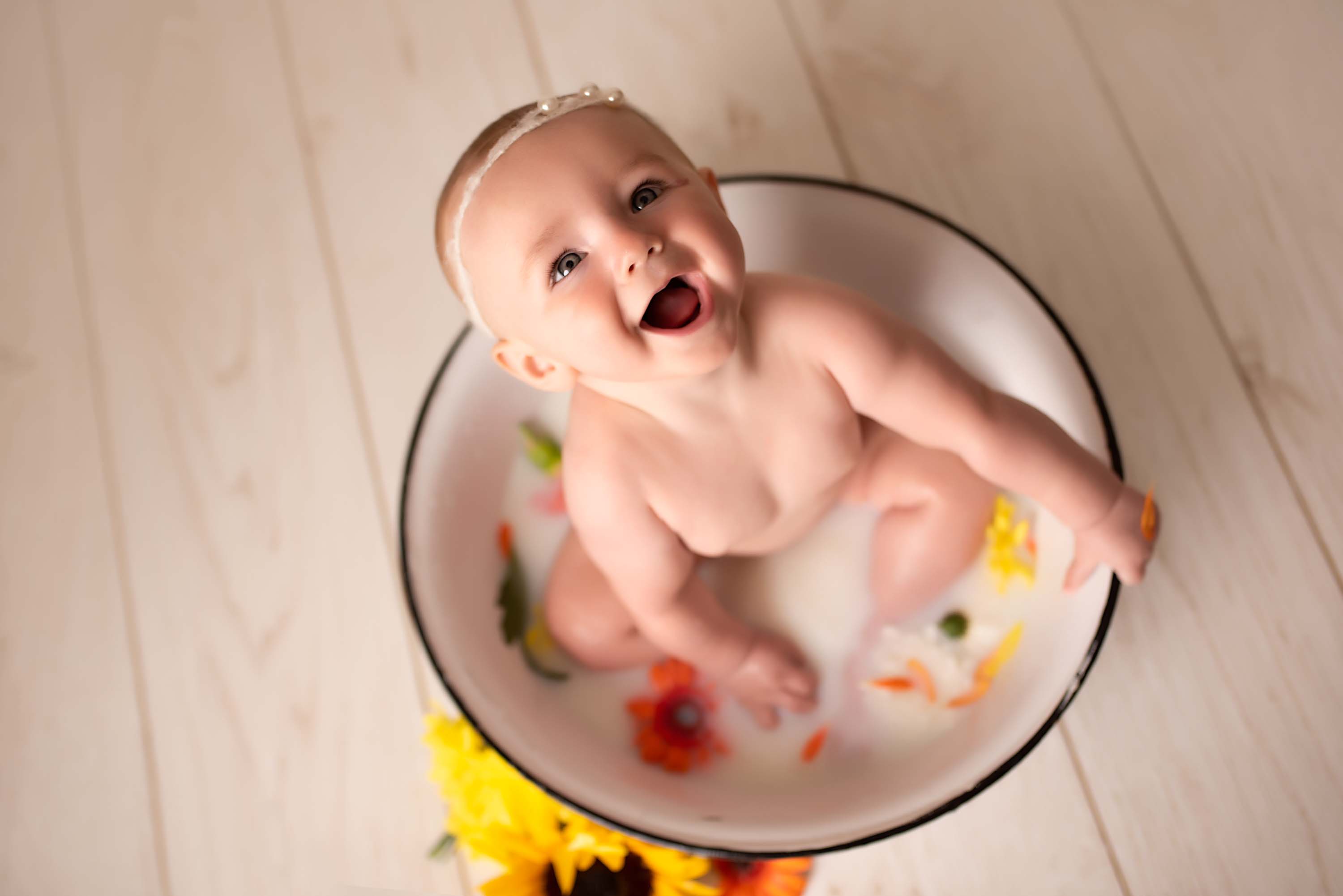Baby girl sitting in a milk bath with flowers for her six month photoshoot