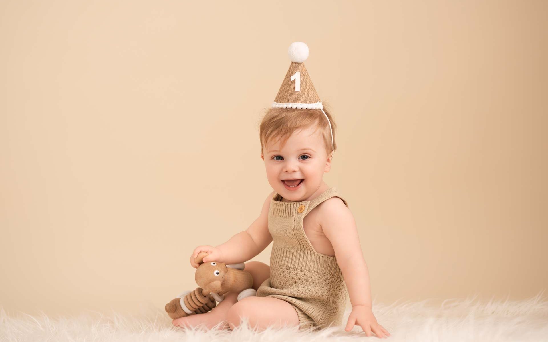 Baby boy with big smile on his face wearing a party hat with the number 1 on it