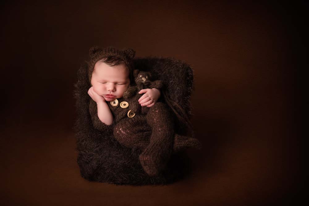 Baby boy cuddling teddy all in brown knitwear