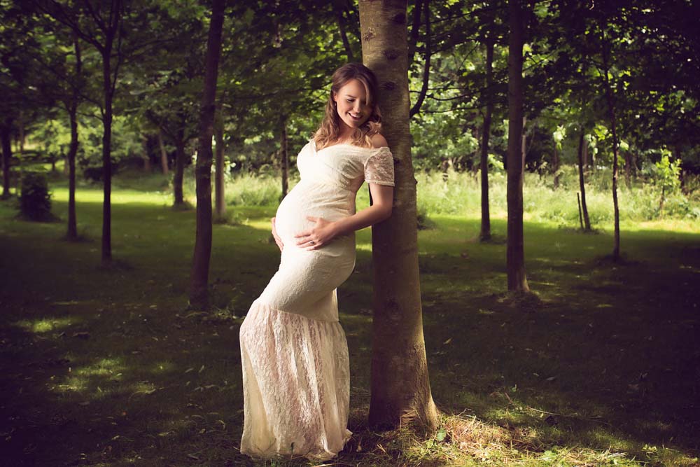 Women with baby bump leaning on a tree outside the family photography studio