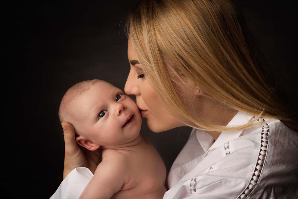 Mother kissing her newborn baby at photoshoot