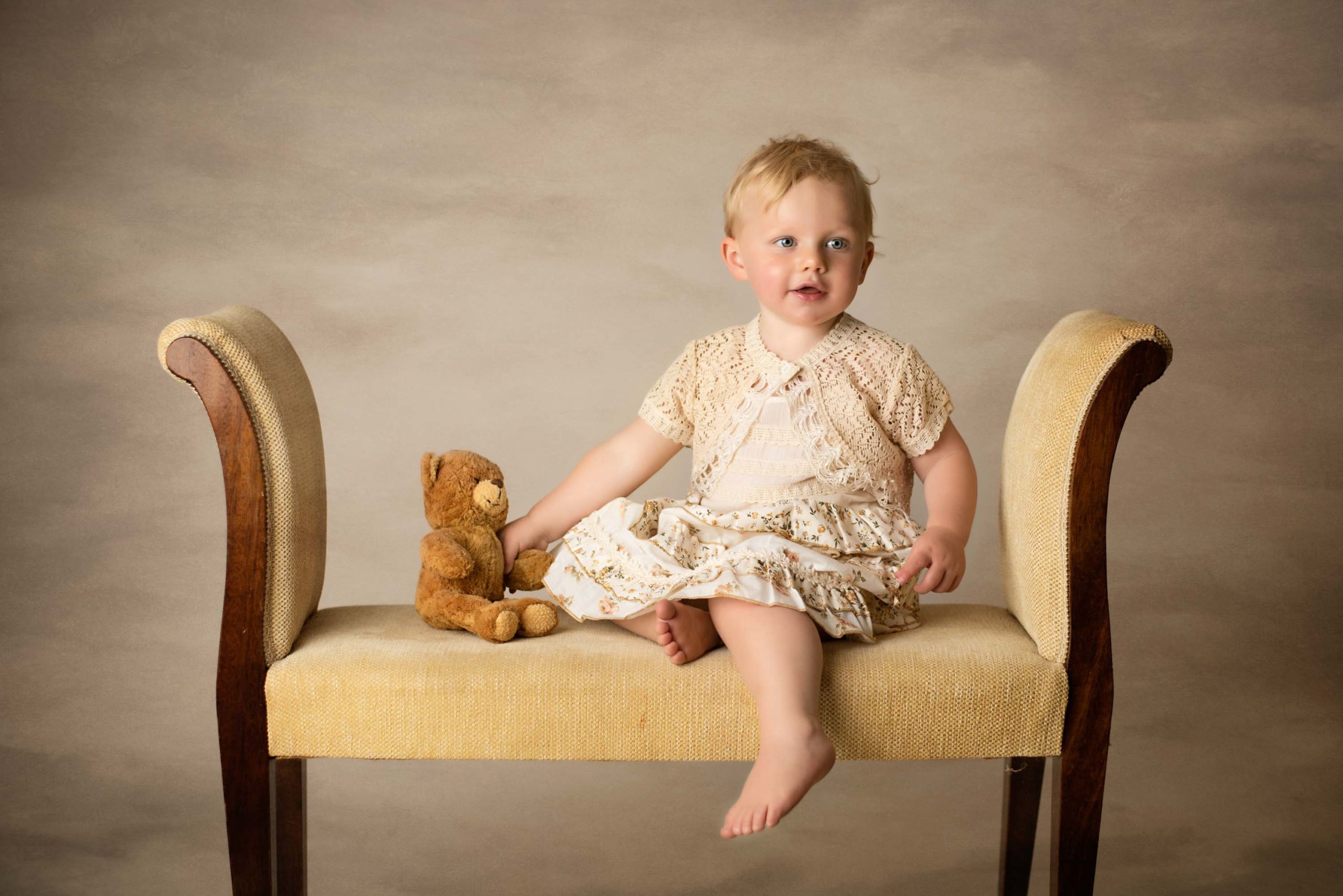 Baby girl sitting on a bench with teddy bear at photoshoot