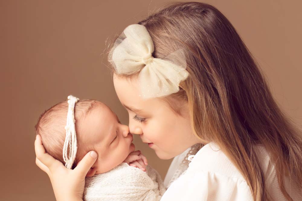 Big sister nose to nose with her new baby sister at their baby photoshoot listening to white noise