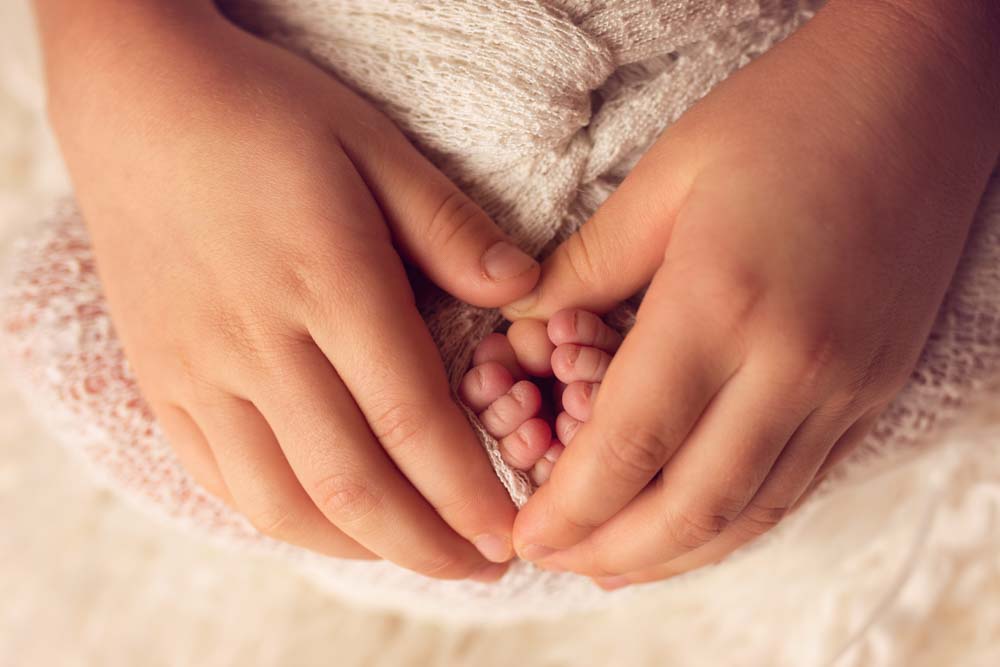 Big sisters hands wrapped around newborn sisters toes