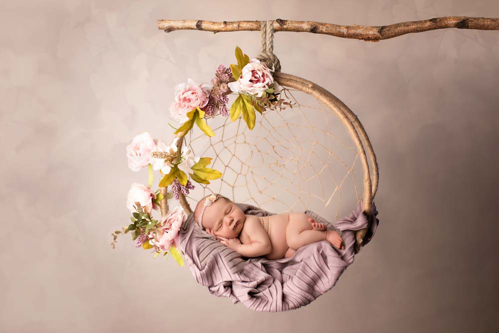 Baby girl asleep in a dreamcatcher decorated with pink peonies