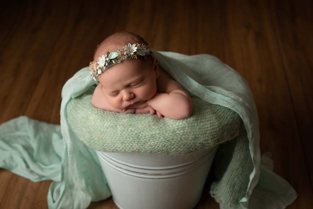 Baby girl asleep in a green themed bucket setup for her newborn photoshoot