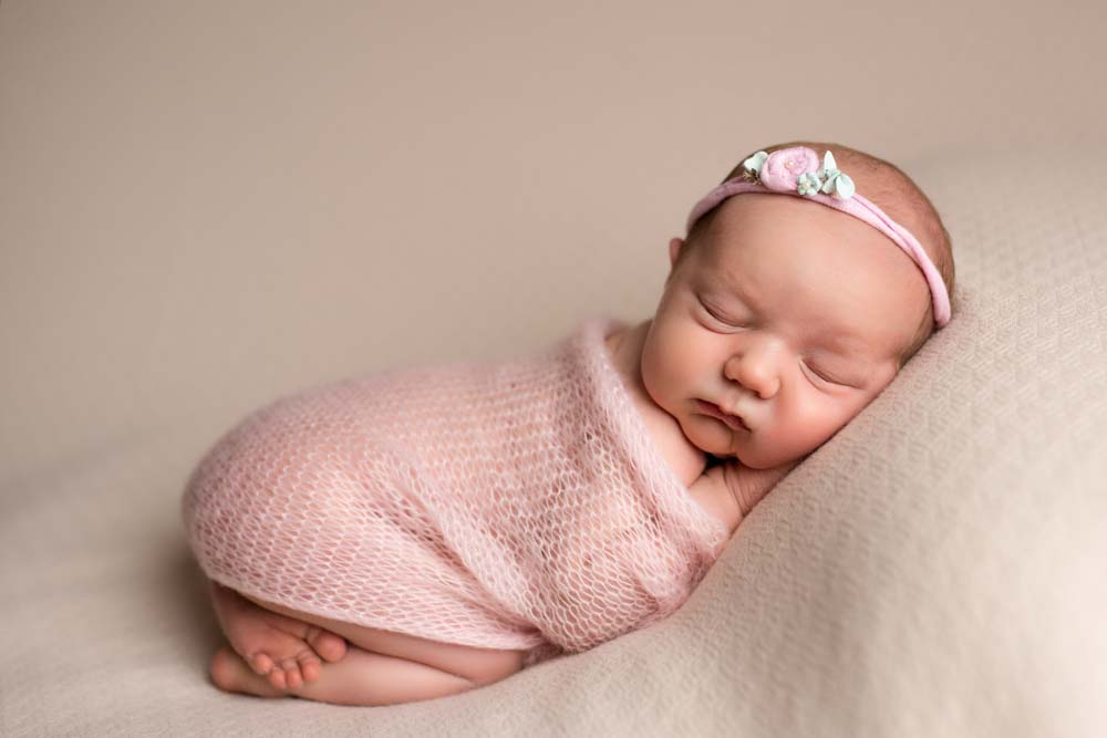 Newborn baby girl sleeping on the photographers beanbag wrapped in a pink cloth