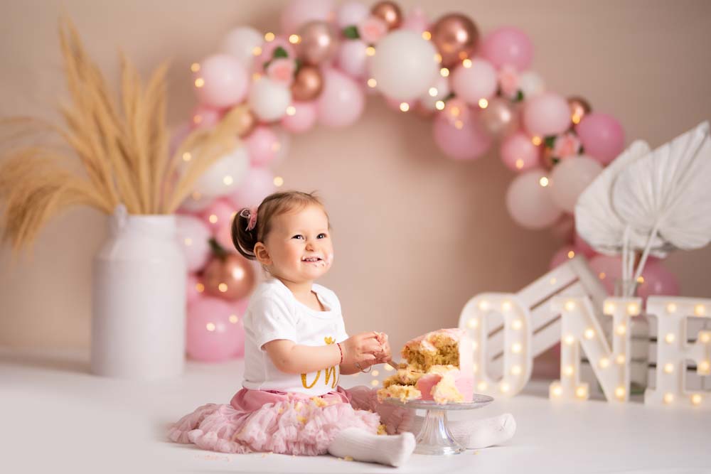 Baby girl destroying her birthday cake at her cake smash photoshoot with a pink and rose gold theme