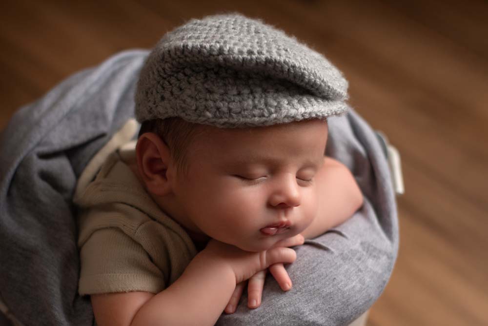 Baby boy being photographed asleep in a bucket wearing a flat cap
