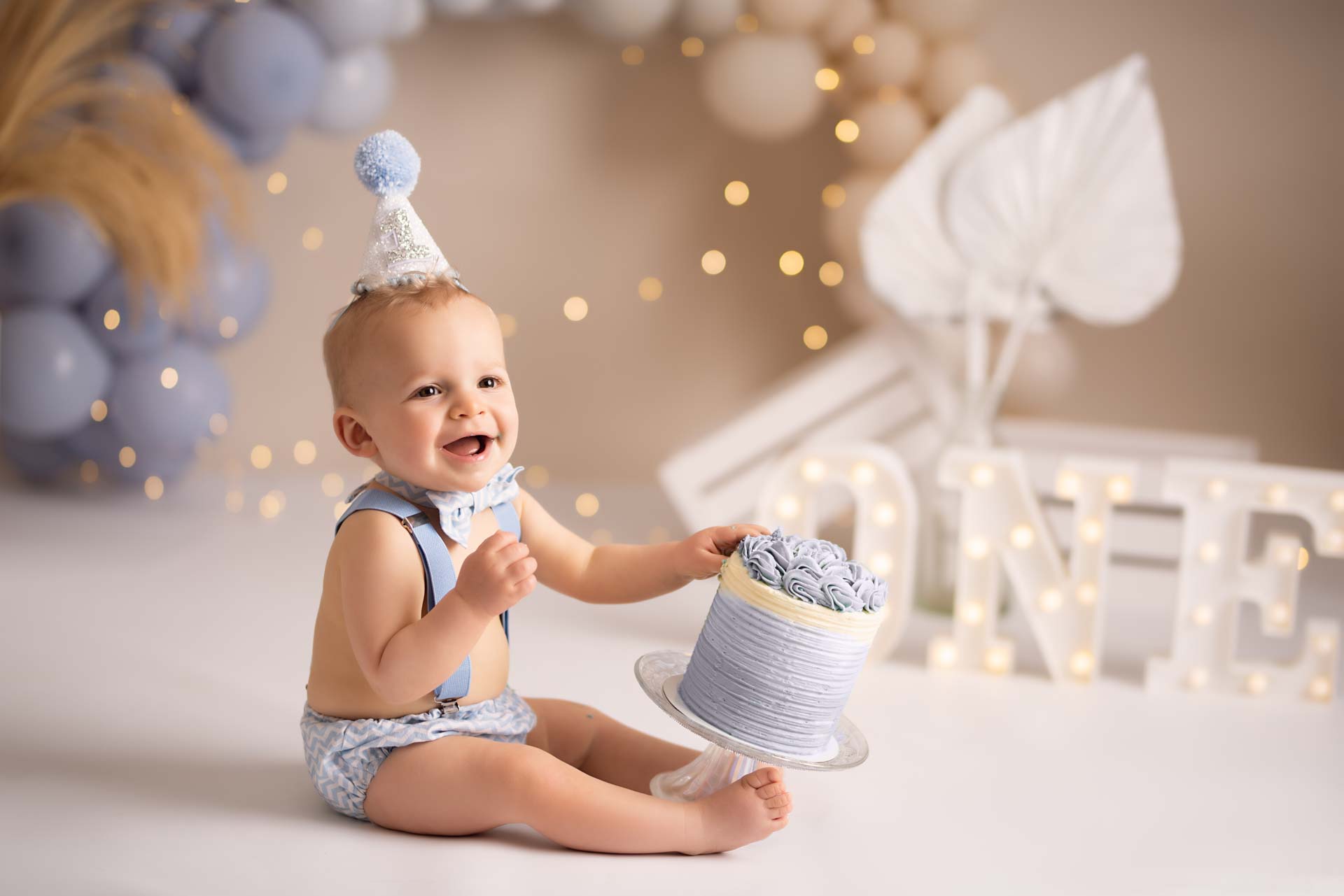 Birthday boy tips his blue cake off it's stand at his photoshoot
