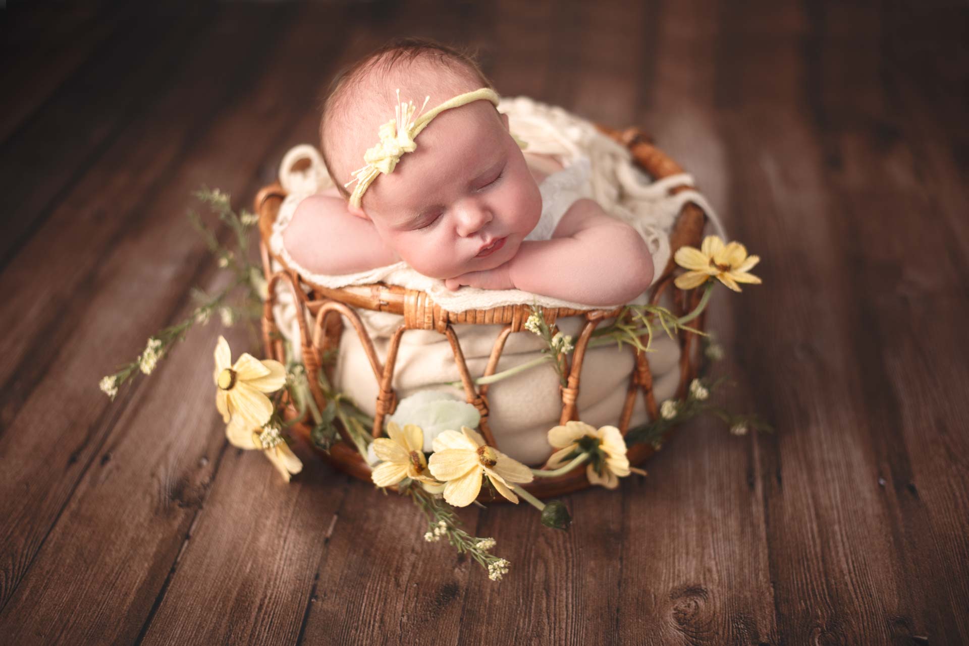 Newborn baby girl resting in a bamboo basket decorated with yellow flowers
