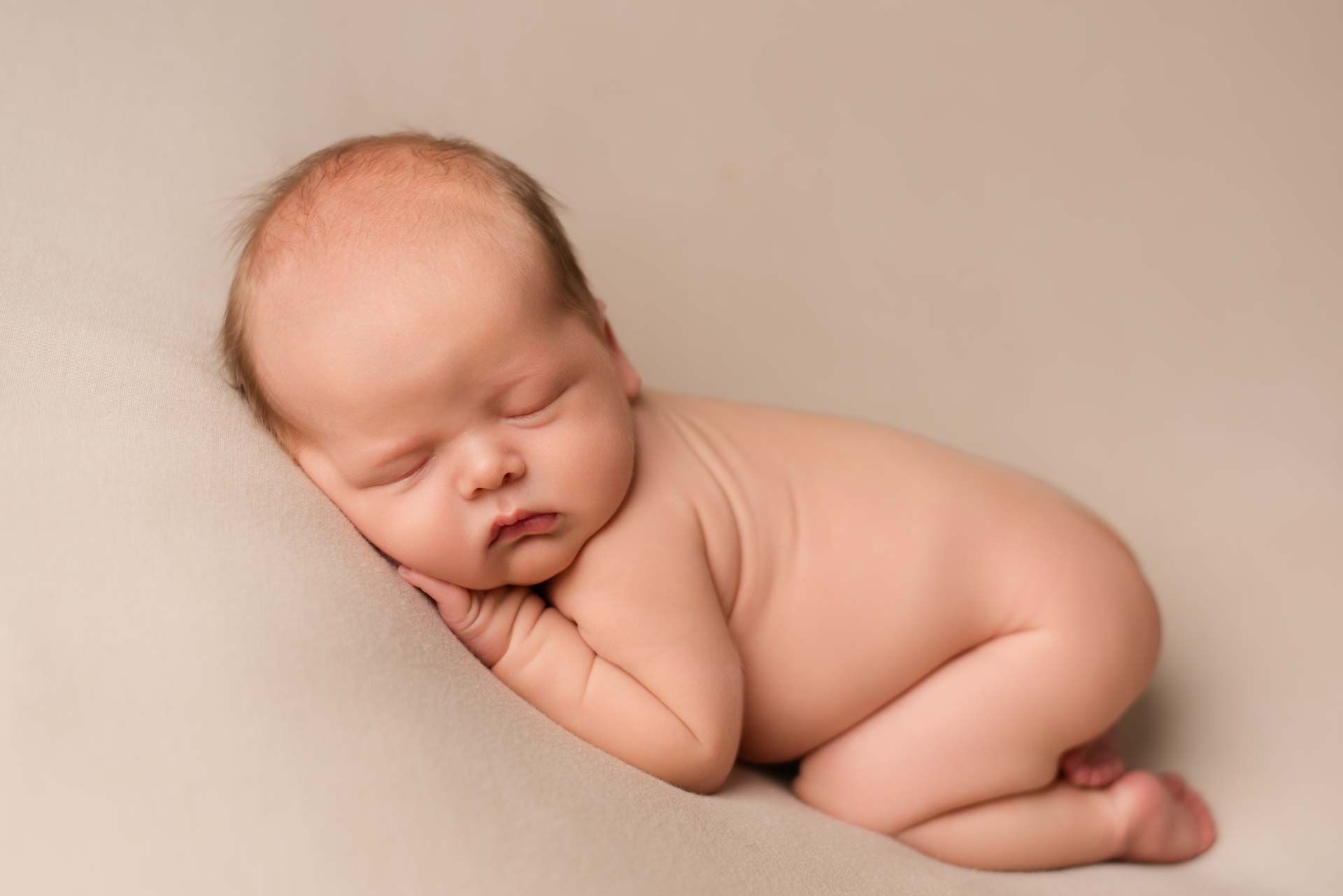 Naked newborn baby boy asleep on a beige blanket