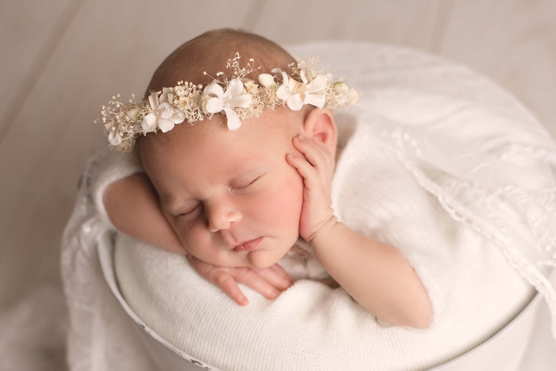 Baby girl posted in a white bucket wearing a delicate white floral headband