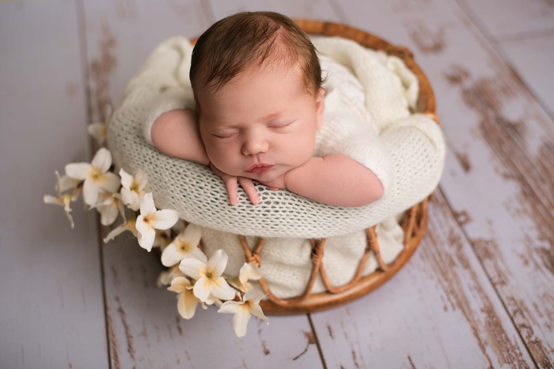 Baby asleep in a bamboo basket on distressed white floorboards