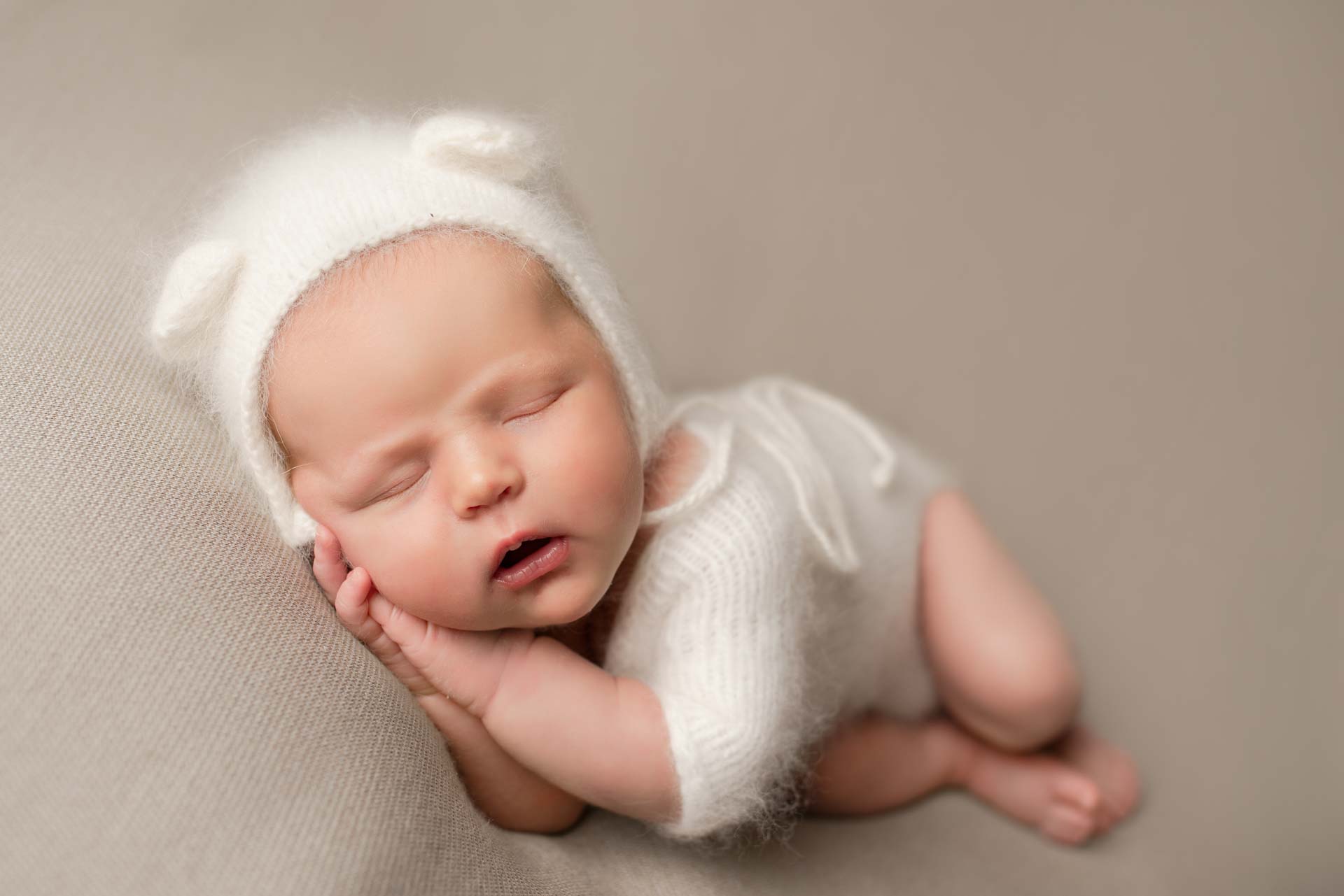 Newborn baby asleep wearing knitted bonnet with bear ears
