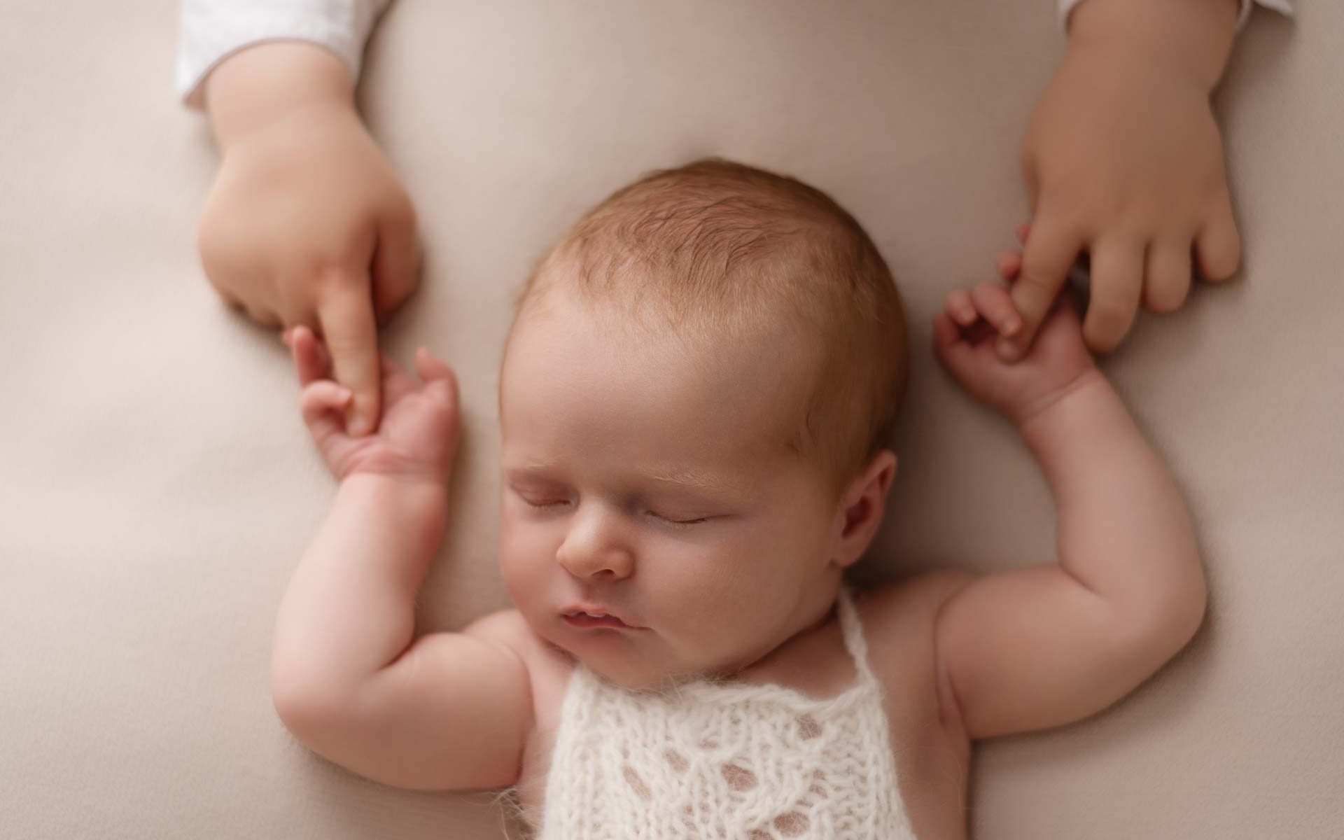 Two year old boy holds his baby daughter's hands during their photoshoot