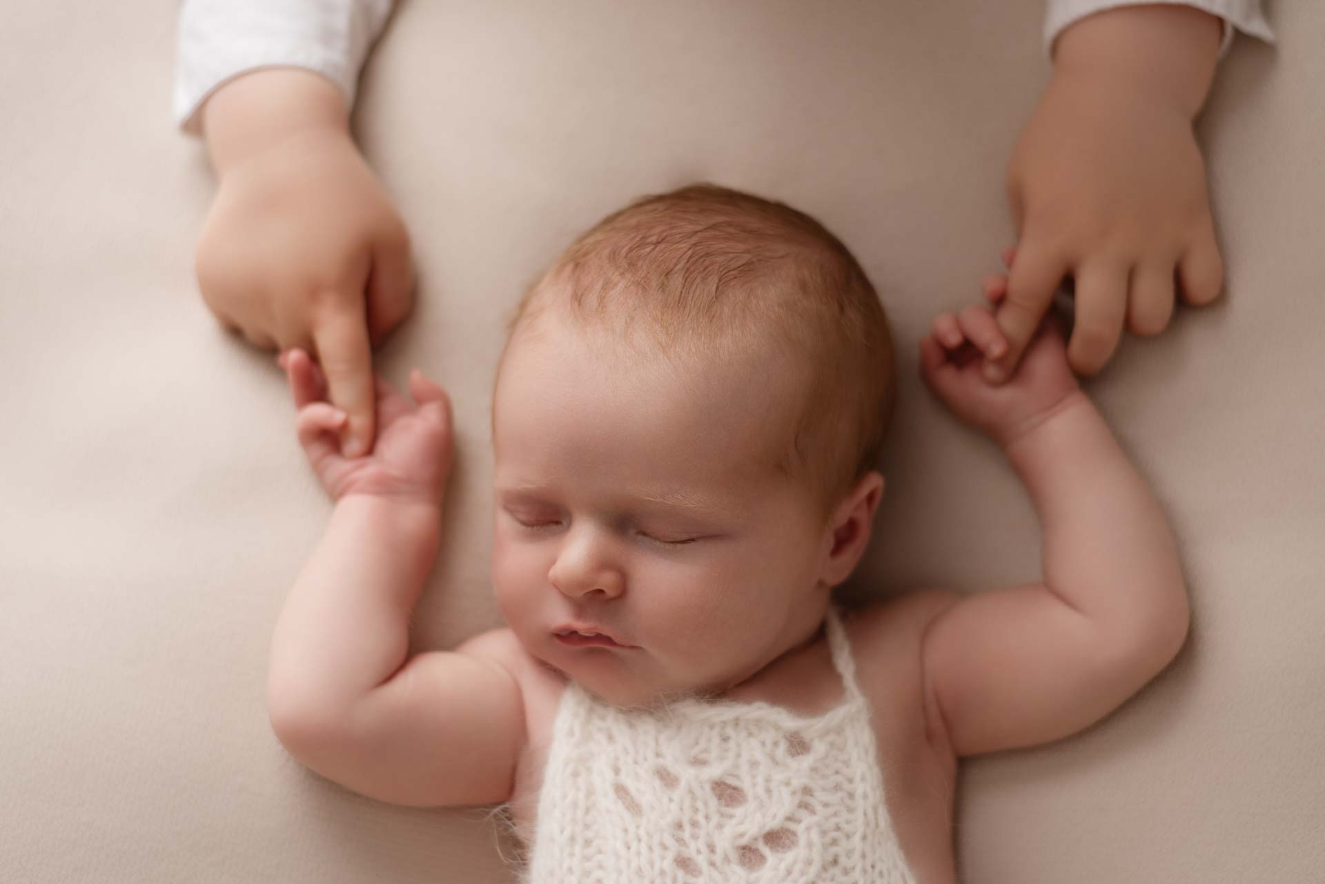 Two year old boy holds his baby daughter's hands during their photoshoot