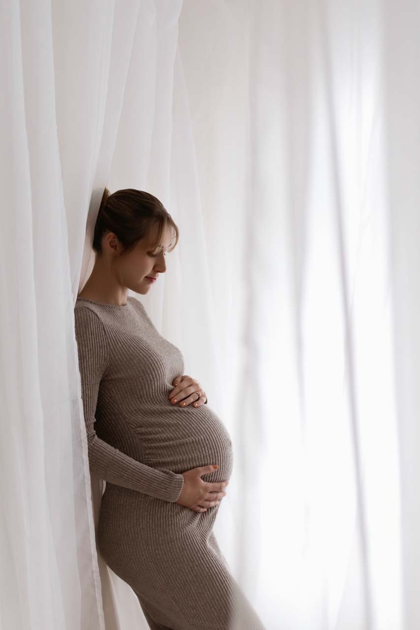 Pregnant women looking at her bump surrounded by flowing net curtains.