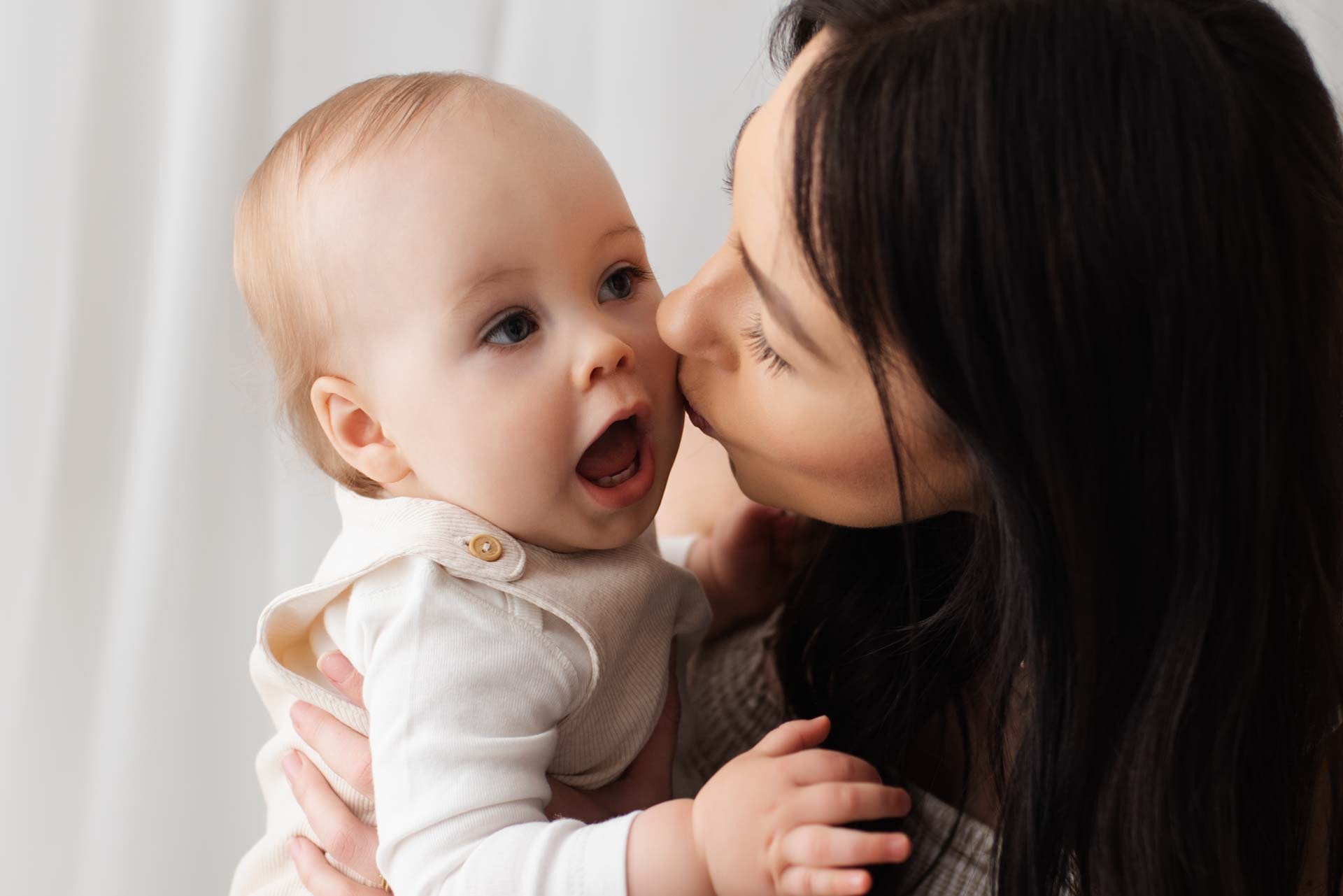 A mother is kissing her son on the cheek. He has his mouth open.