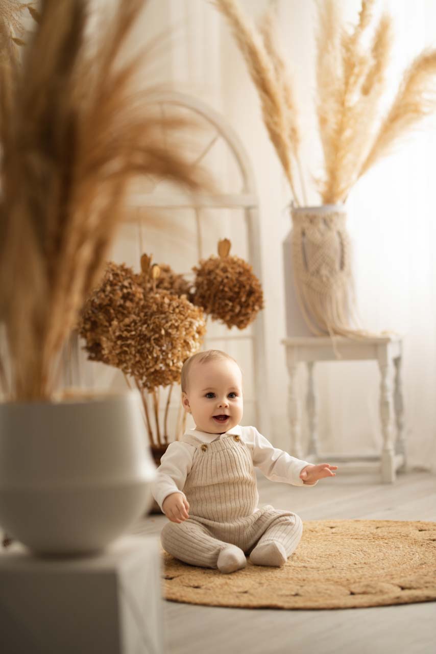 Baby boy sitting on a straw mat. In the background are dried flowers and pampas grass