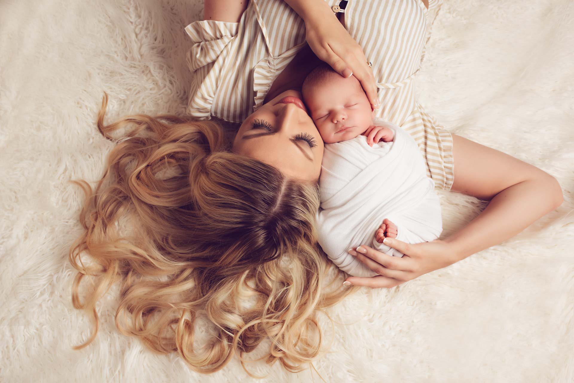 Mother and son lying on a fluffy blanket. The baby is swaddled and placed next to the mother's face.