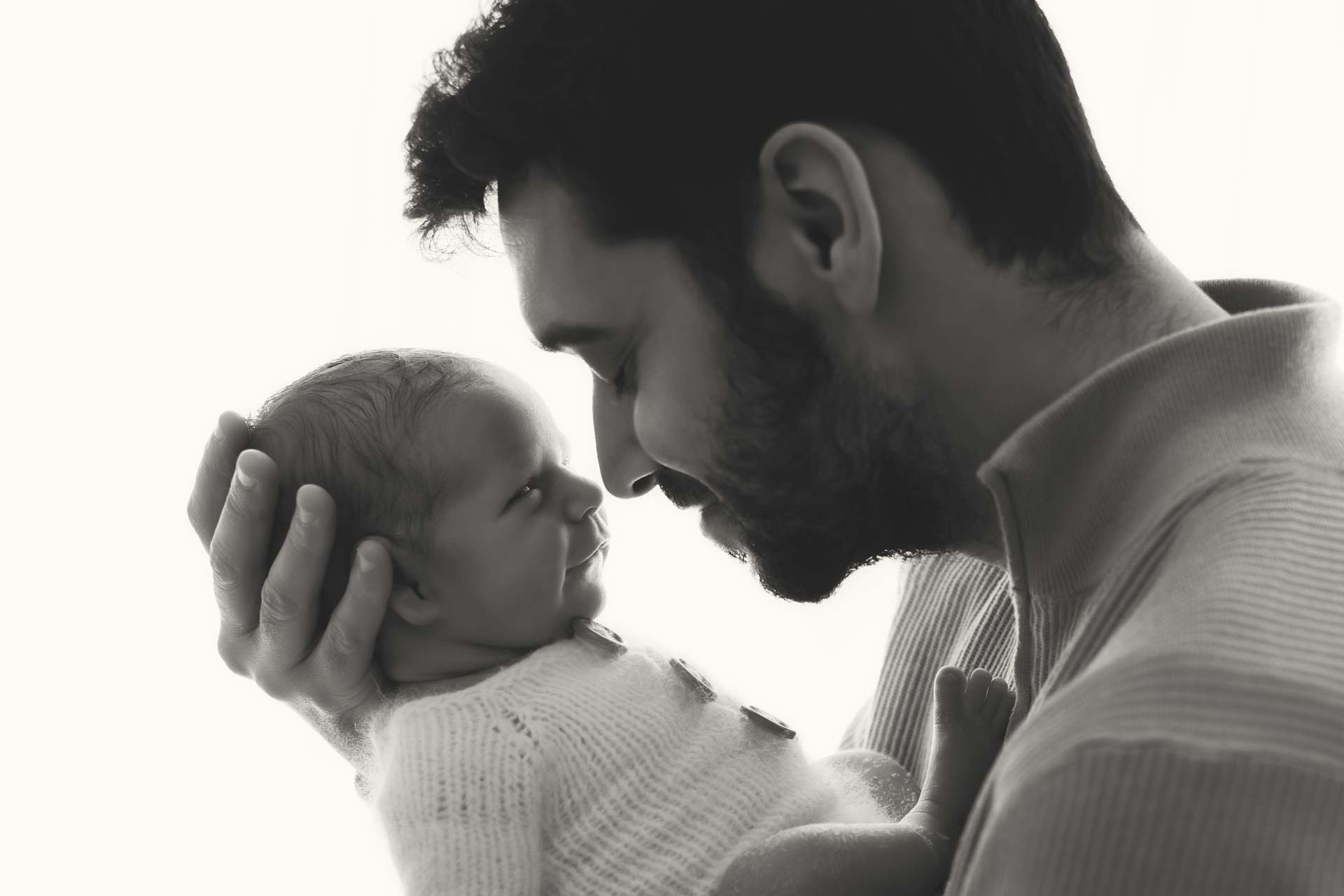 Baby boy smiles at his daddy who is holding him close to his face. The photograph is in black and white