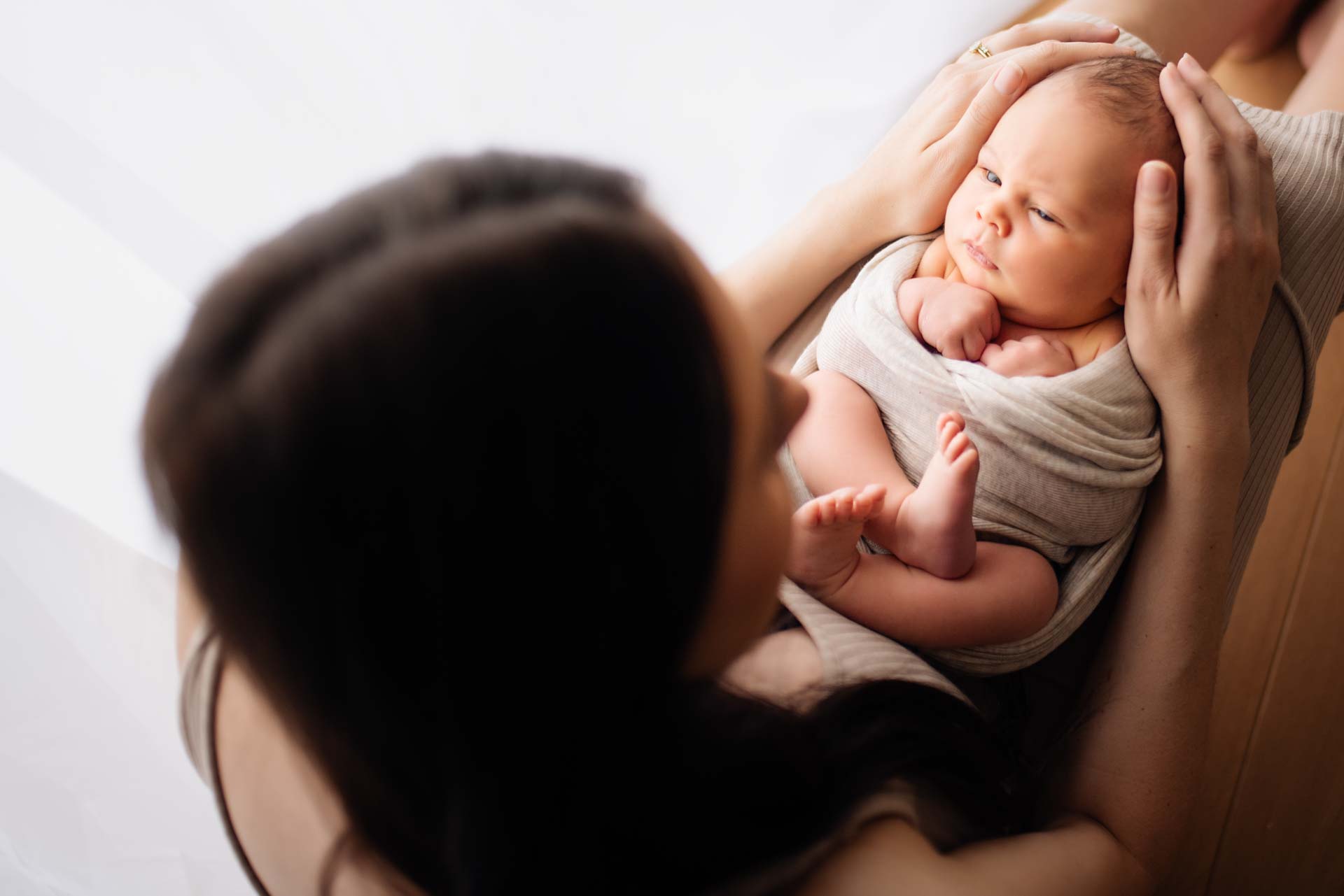 Newborn baby boy staring at his mother swaddled on her legs