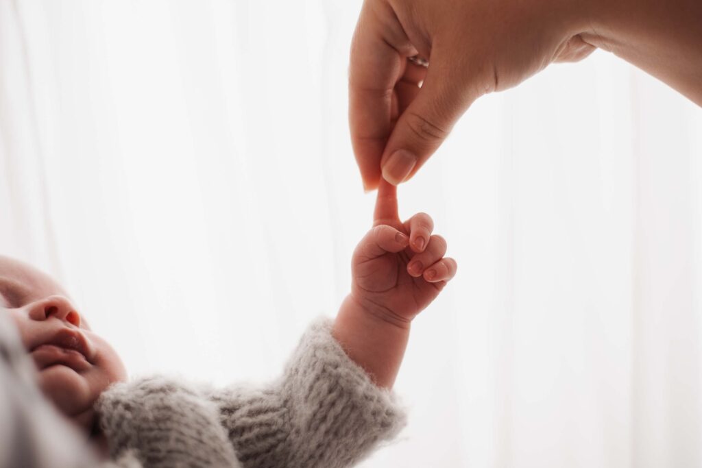 Mother holding her newborn baby's finger aloft at her baby studio photoshoot