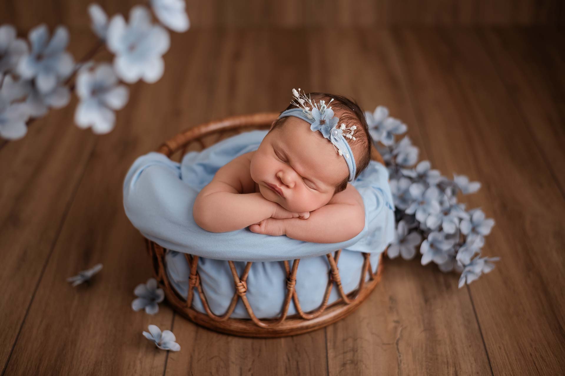 Baby girl with her head resting on her arms posed in a bamboo basket with a blue colour theme