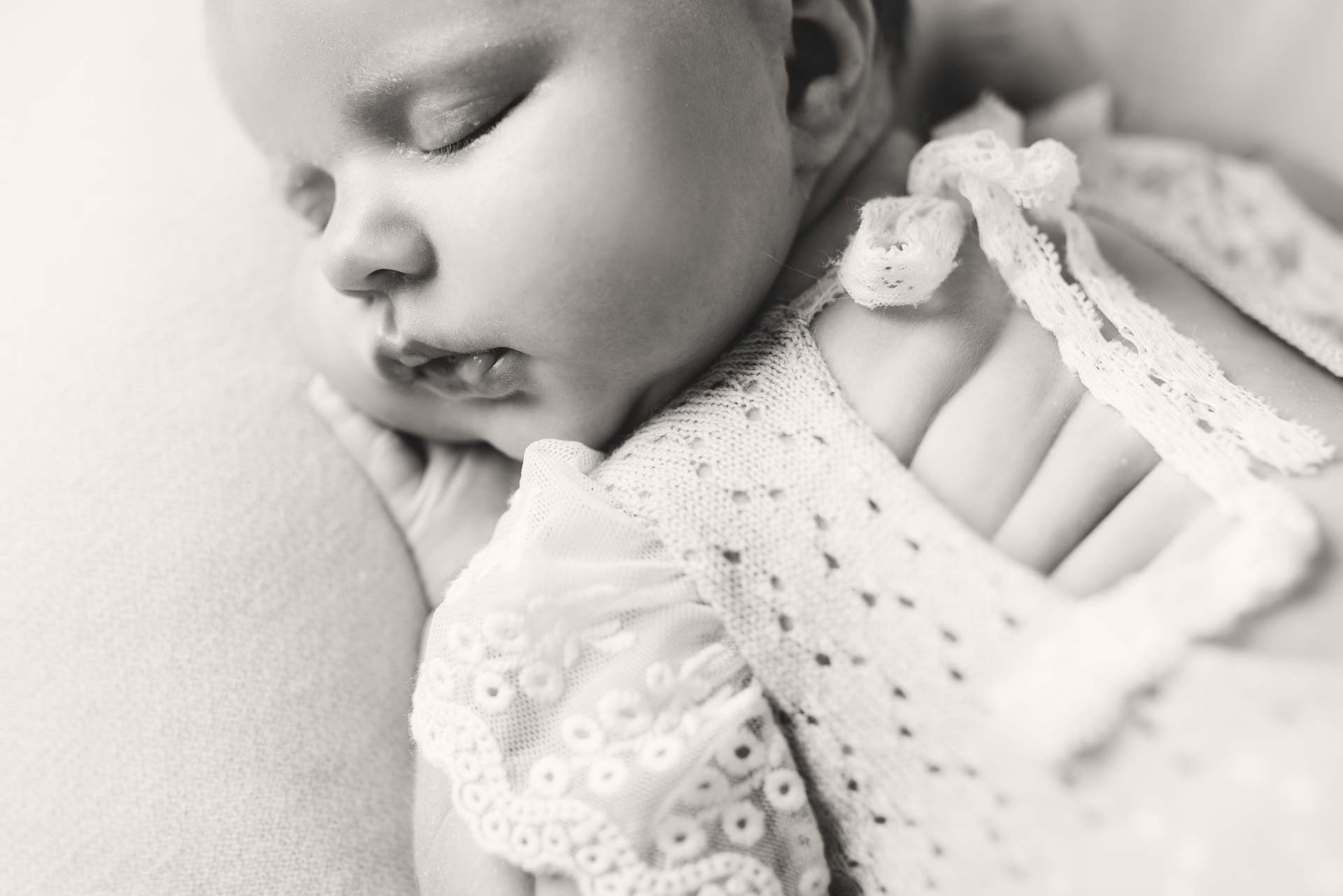 Overhead photo of baby girl wearing a lace romper showing her the fat rolls on her back. The photo is black and white
