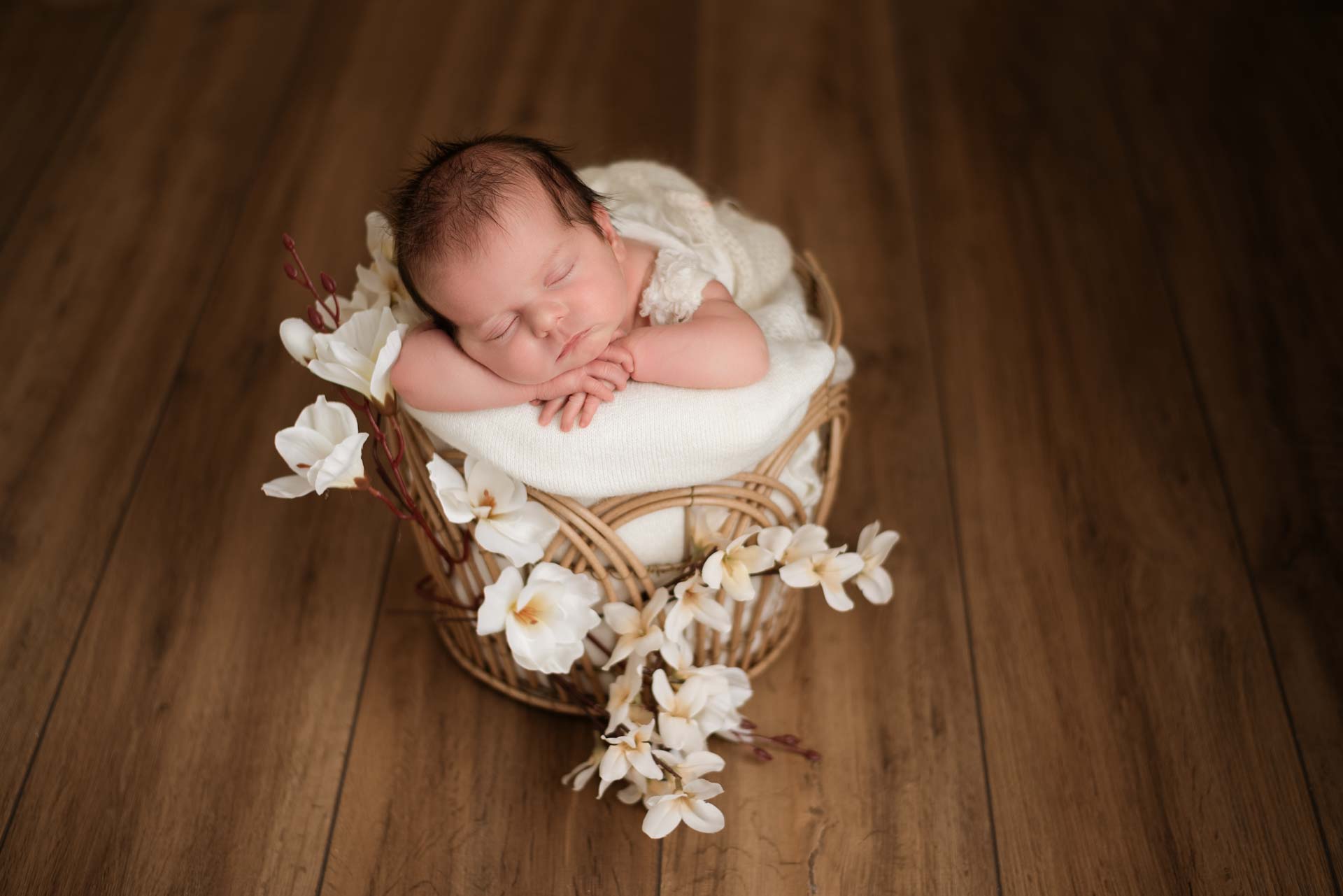 Baby girl posed in a wicker basket decorated with white orchids